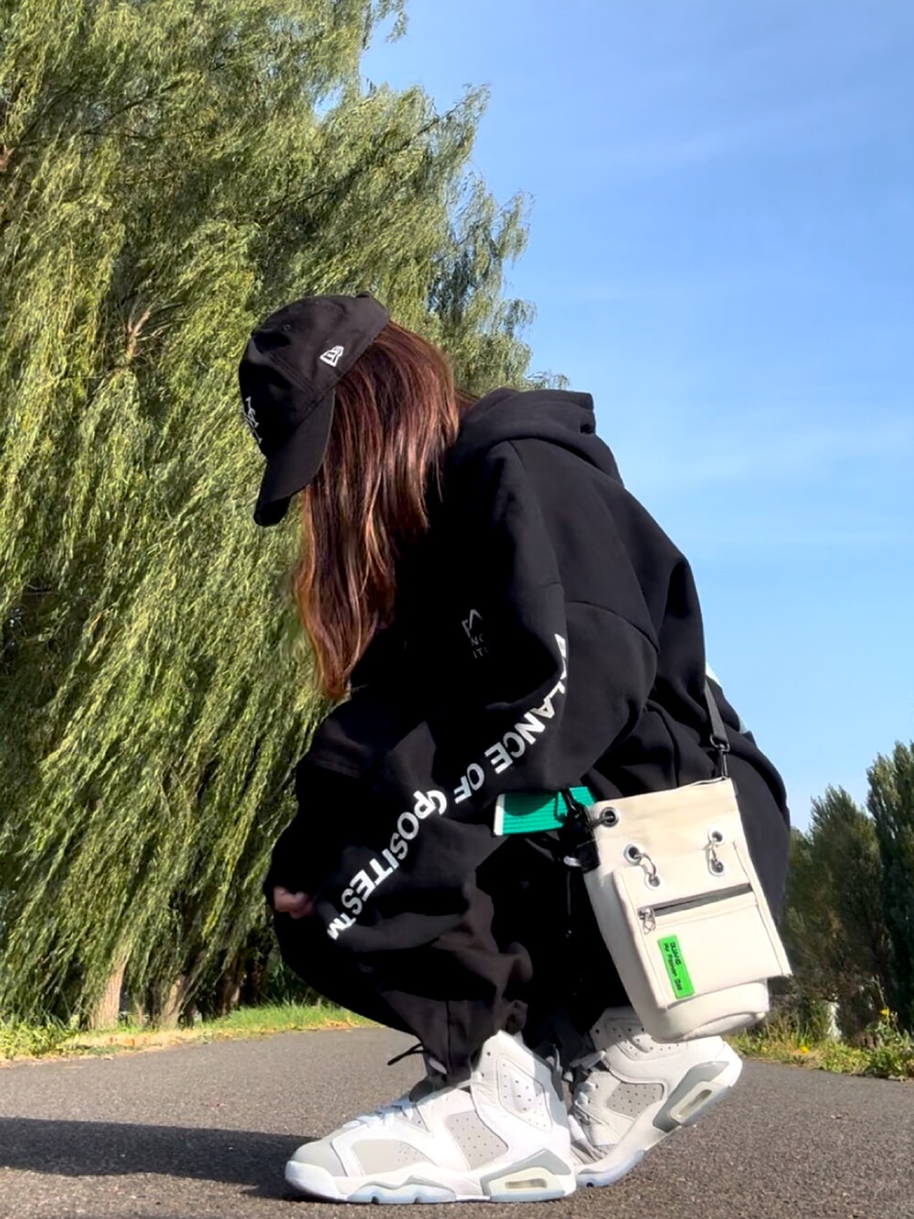 ブラック系のパーカー、ホワイト系のスニーカー、ホワイト系のショルダーバッグを着用したレディースの秋コーディネートの3枚目の写真