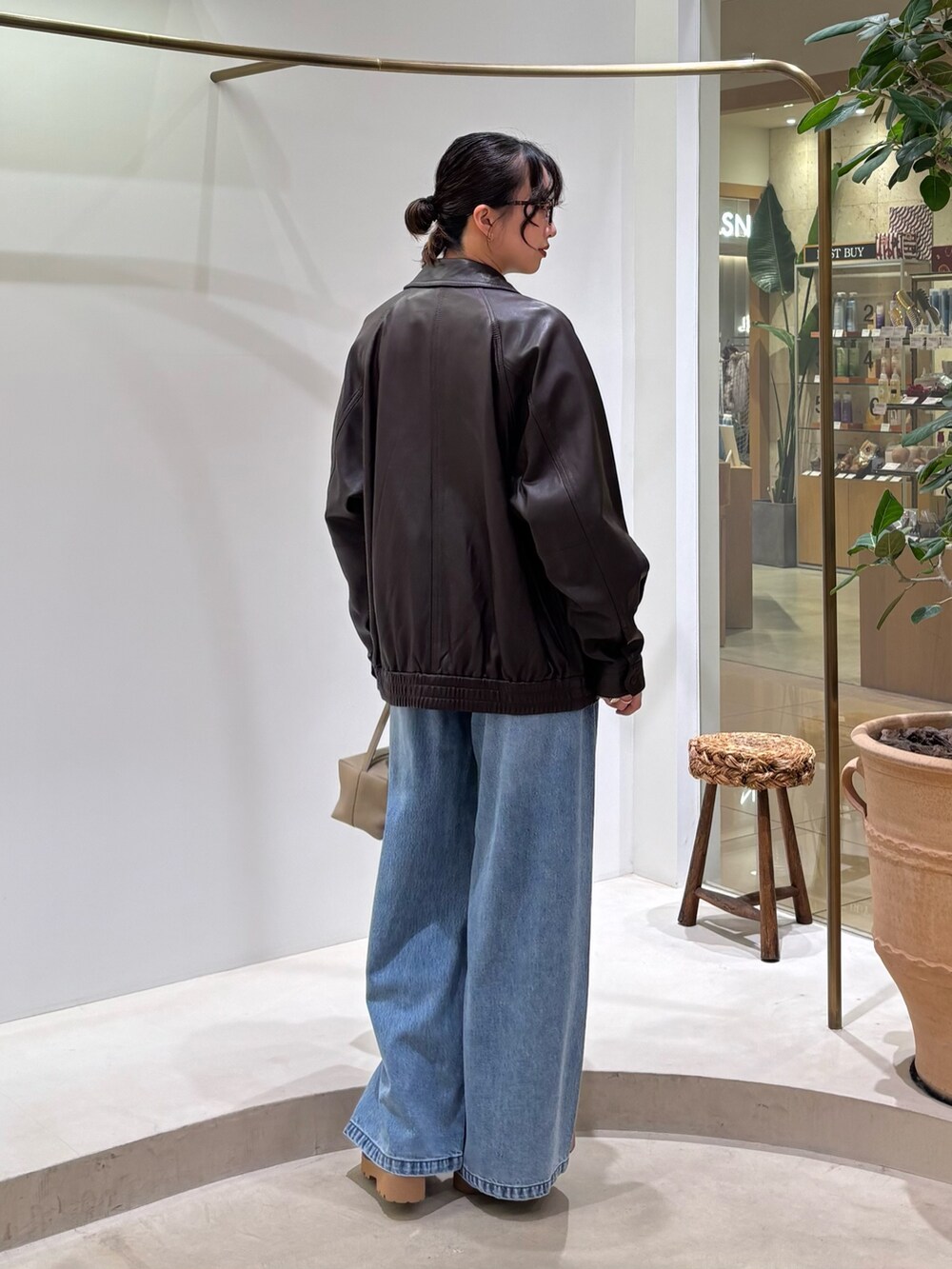 ブラウン系のブルゾン、ホワイト系のニット/セーター、ブルー系のデニムパンツを着用したレディースの秋コーディネートの4枚目の写真