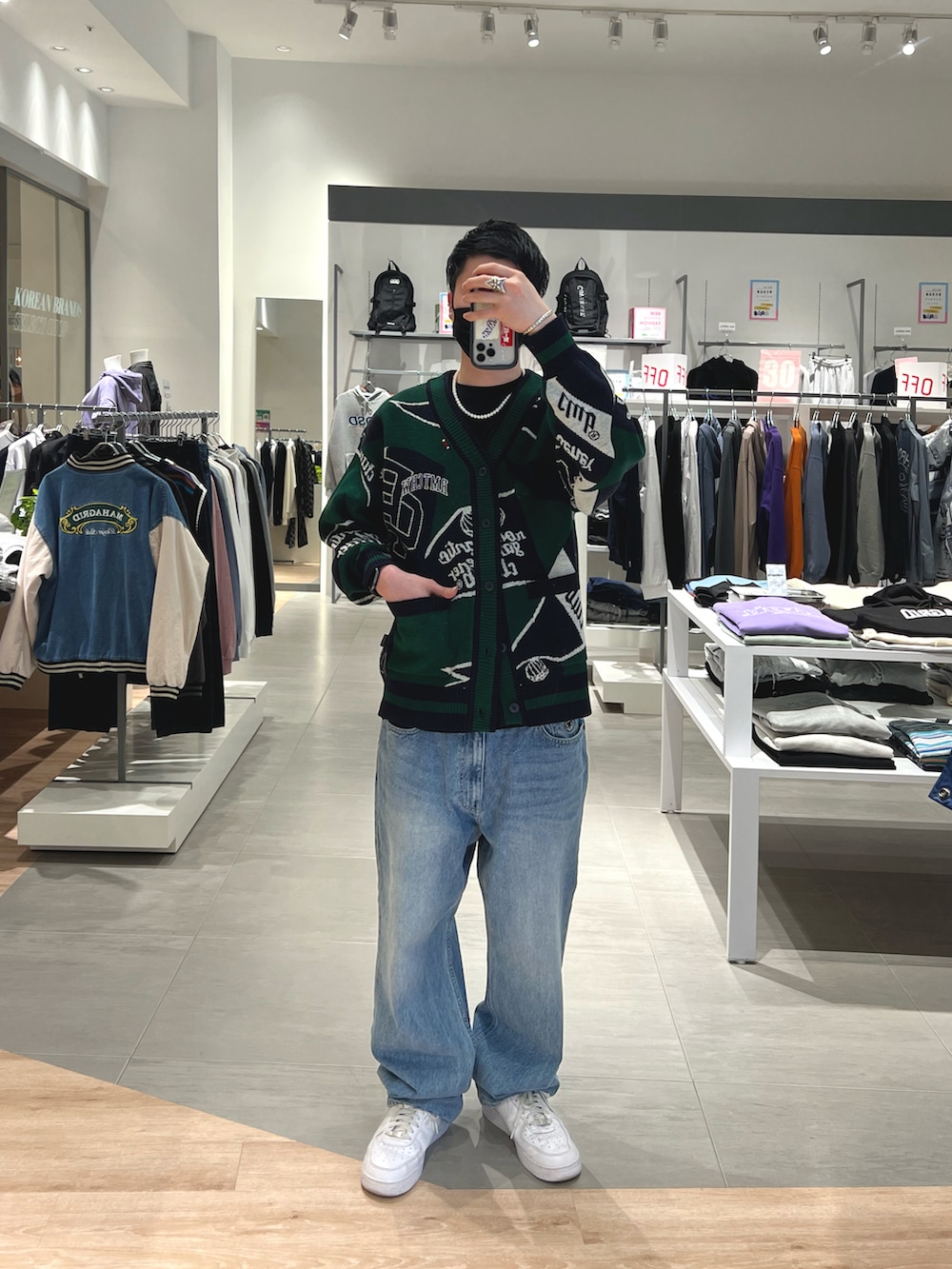 グリーン系のカーディガン/ボレロ、ブルー系のデニムパンツ、ホワイト系のスニーカーを着用したメンズの春コーディネートの2枚目の写真