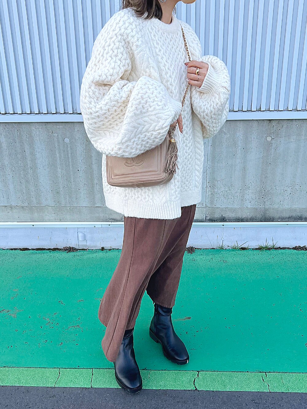 ホワイト系のニット/セーター、ブラウン系のスカート、ブラック系のブーツを着用したレディースの冬コーディネートの2枚目の写真