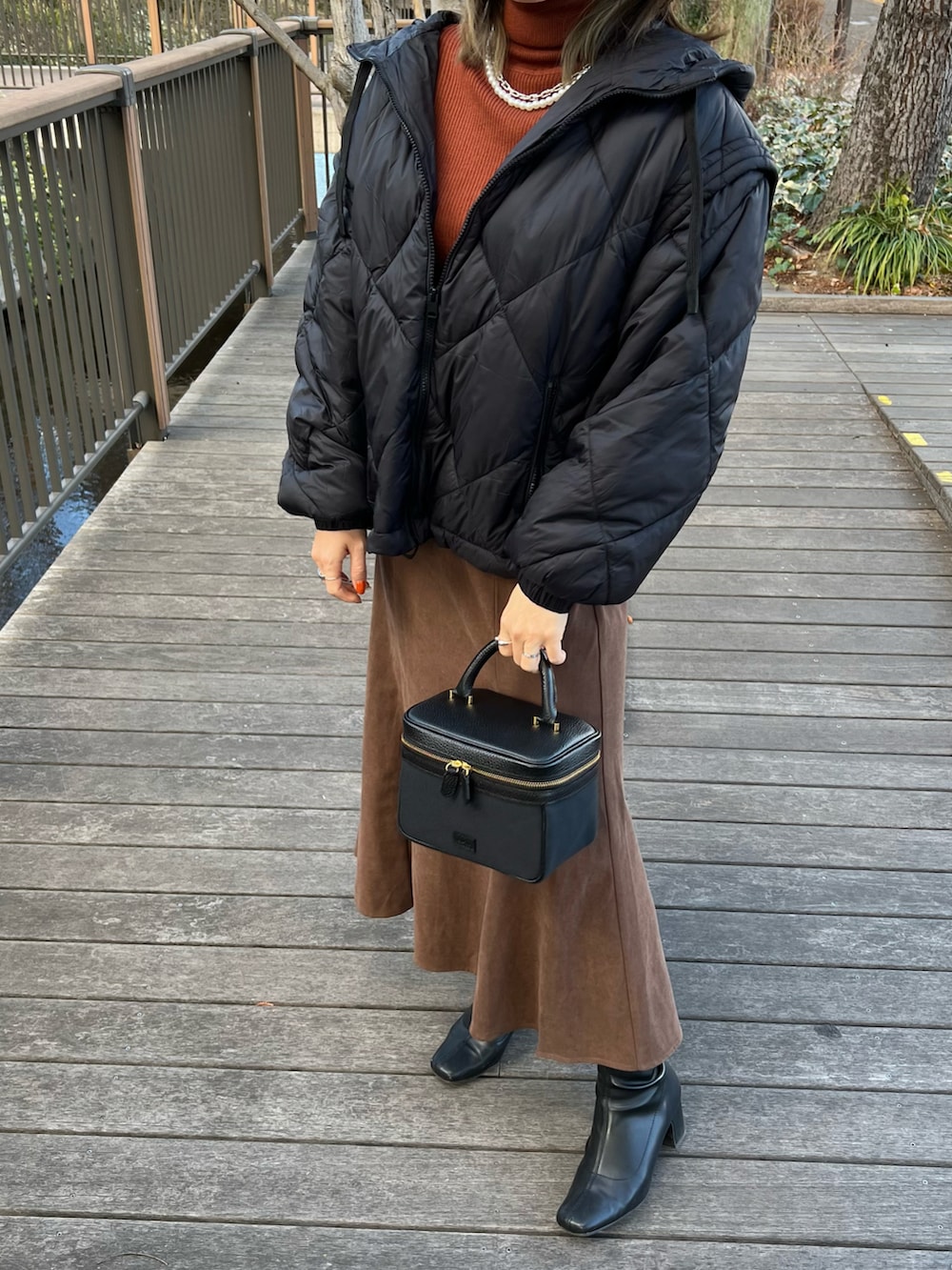 ブラウン系のスカート、ブラック系のブーツ、ブラック系のハンドバッグを着用したレディースの冬コーディネートの2枚目の写真