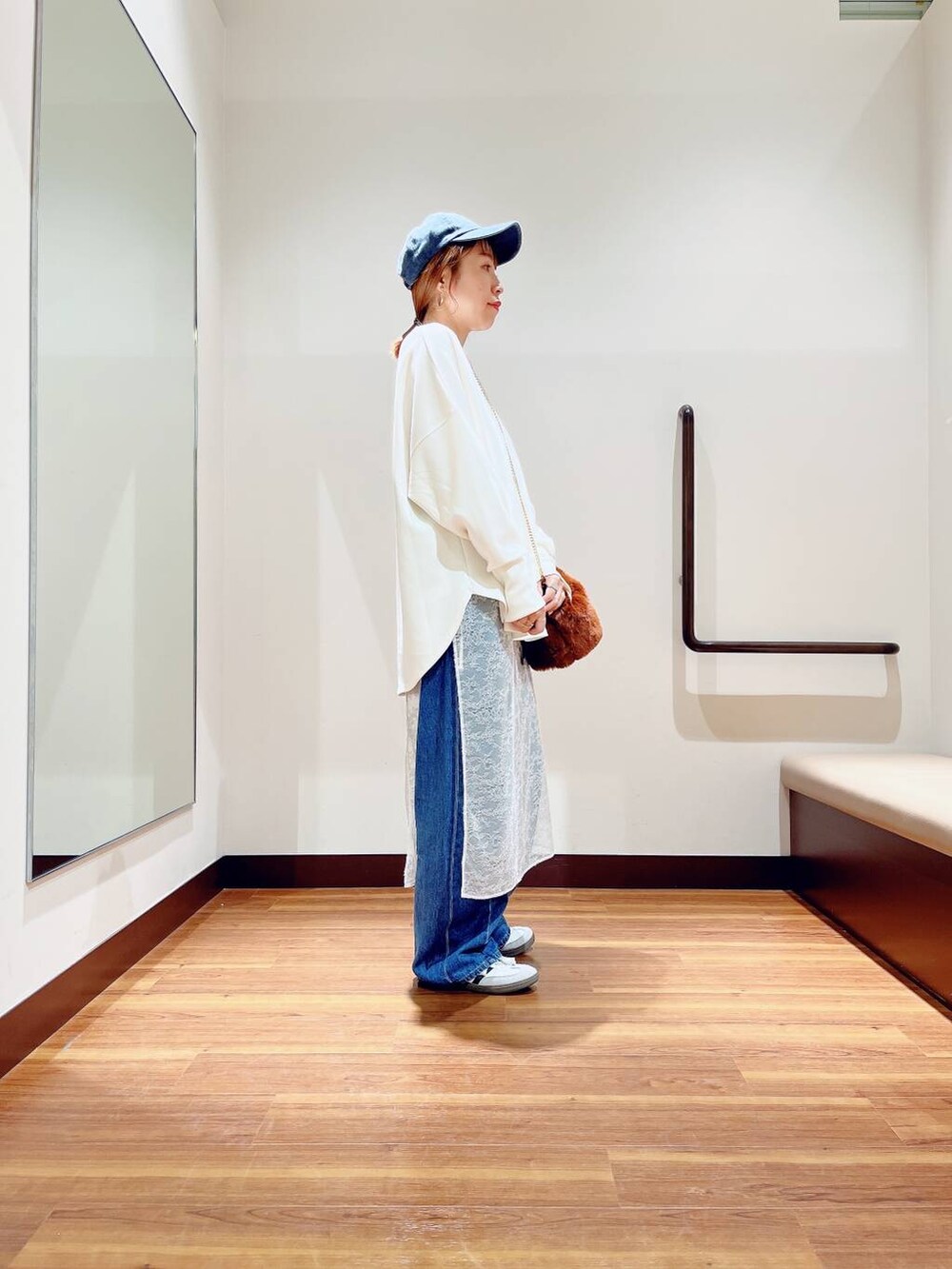 ブラウン系のショルダーバッグ、ブルー系のデニムパンツ、ホワイト系のスカートを着用したレディースの秋コーディネートの3枚目の写真