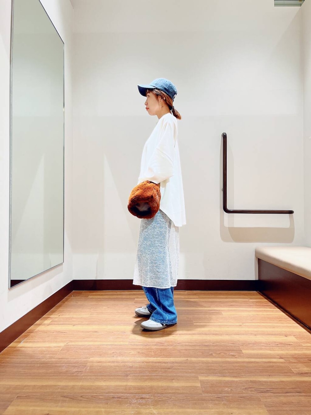 ブラウン系のショルダーバッグ、ブルー系のデニムパンツ、ホワイト系のスカートを着用したレディースの秋コーディネートの2枚目の写真