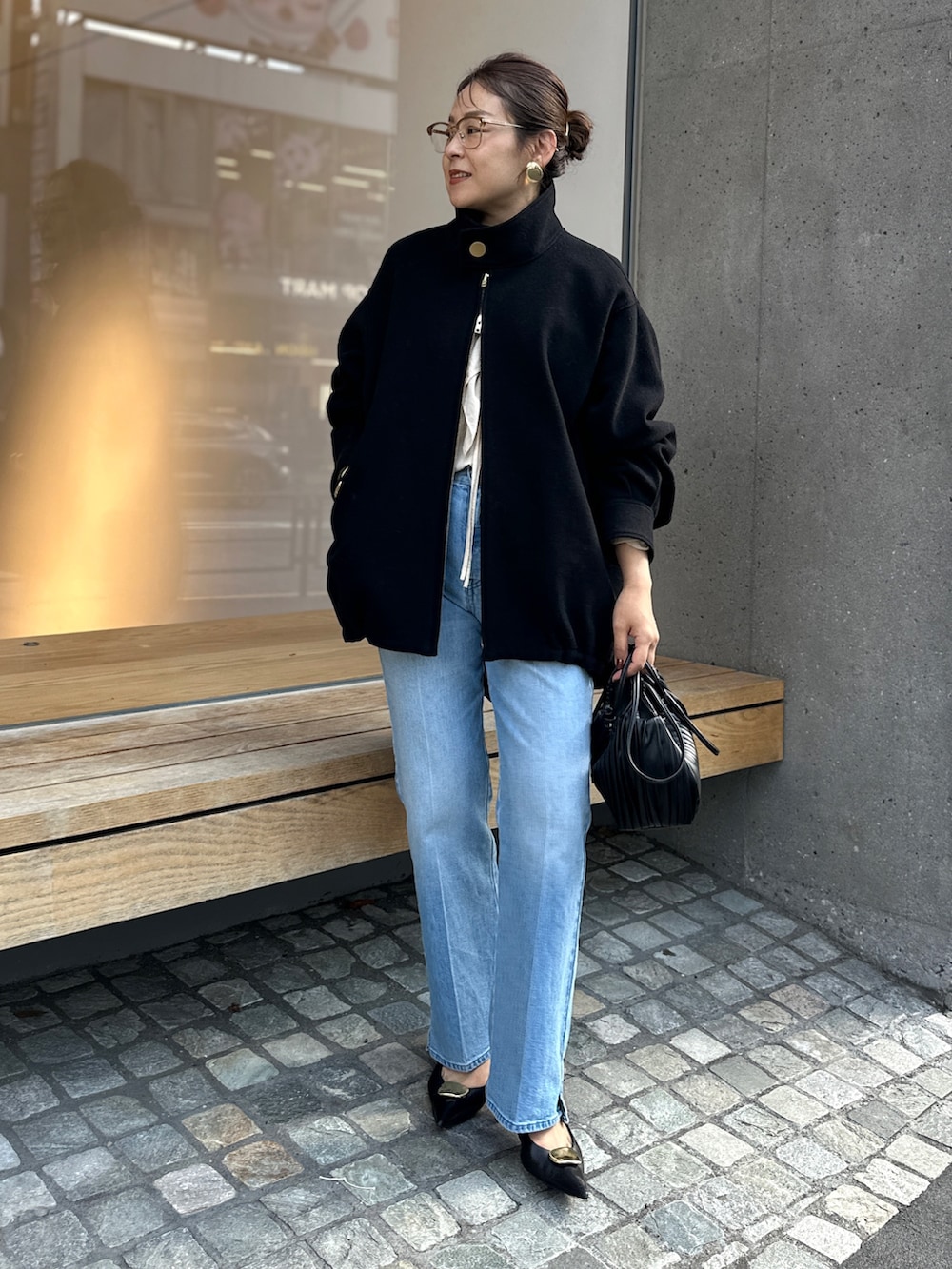 ブラック系のチェスターコート、ブルー系のデニムパンツ、ベージュ系のシャツ/ブラウスを着用したレディースの秋コーディネートの2枚目の写真
