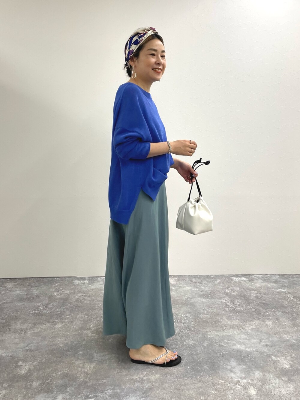 ブルー系のニット/セーター、ブルー系のスカート、ホワイト系のショルダーバッグを着用したレディースの春コーディネートの2枚目の写真