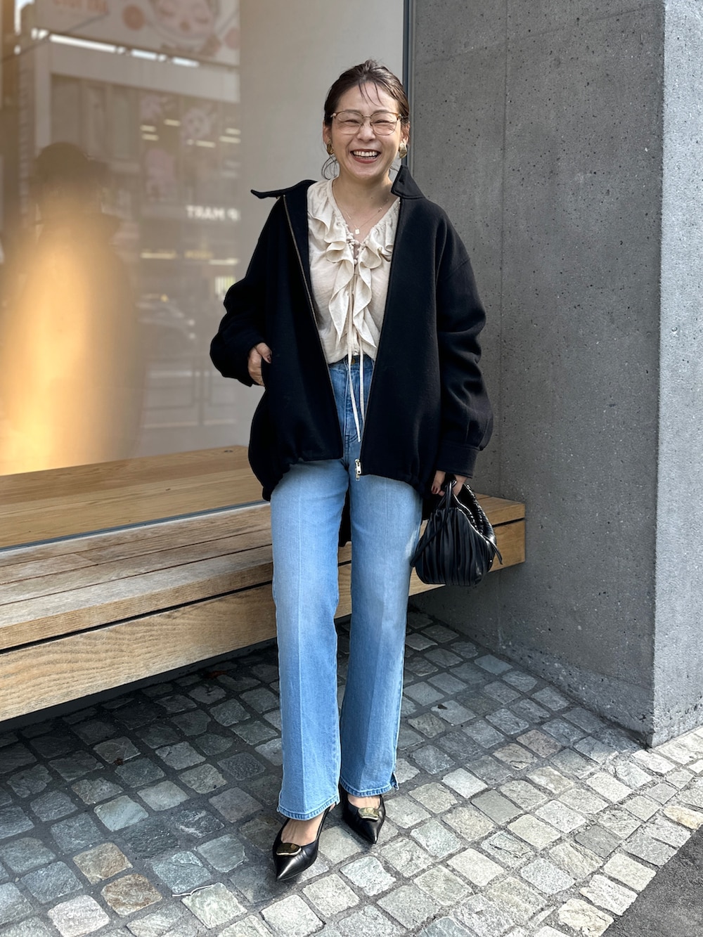 ブラック系のチェスターコート、ブルー系のデニムパンツ、ベージュ系のシャツ/ブラウスを着用したレディースの秋コーディネートの5枚目の写真