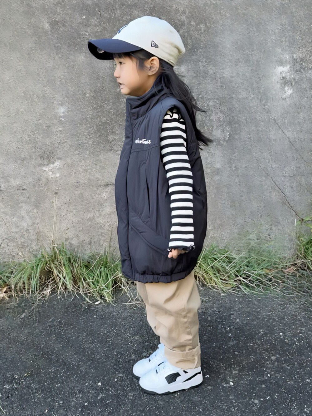 ブラック系のダウンベスト、ブラック系のトップス、ベージュ系のチノパンツを着用したキッズの冬コーディネートの2枚目の写真