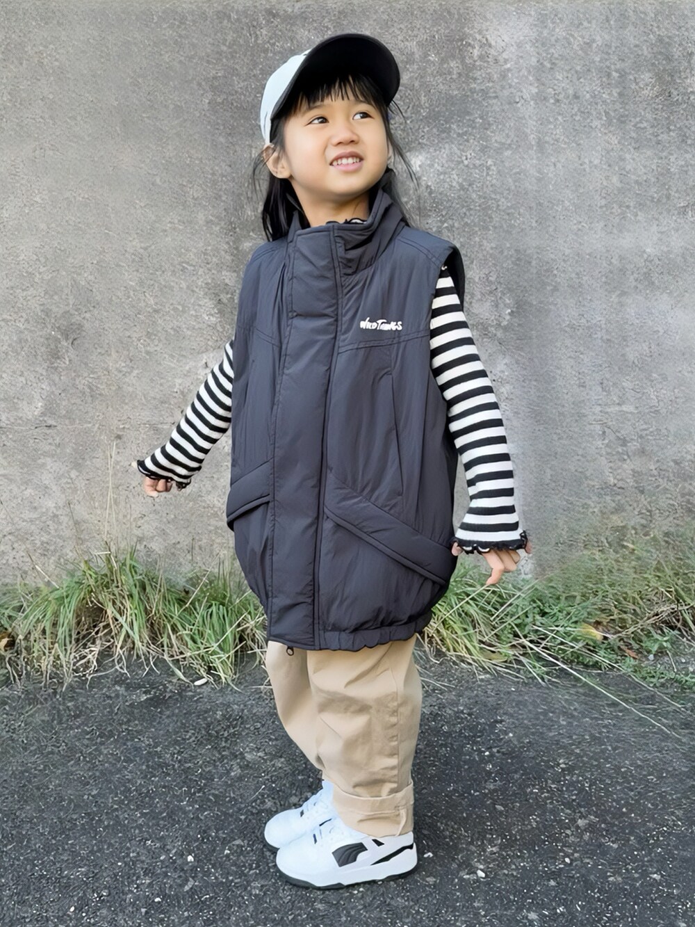 ブラック系のダウンベスト、ブラック系のトップス、ベージュ系のチノパンツを着用したキッズの冬コーディネートの3枚目の写真