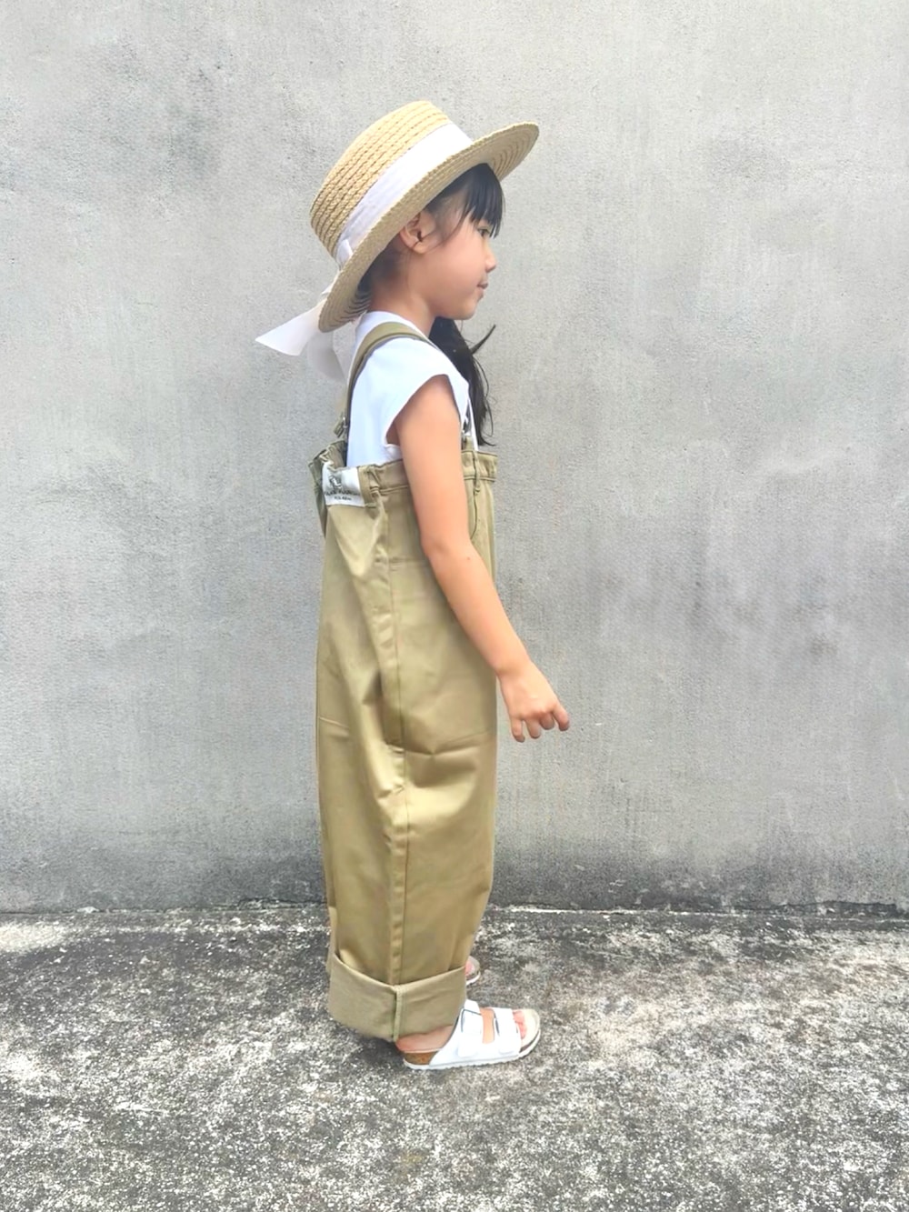 ベージュ系のサロペット/オーバーオール、ホワイト系のサンダル、ベージュ系のハットを着用したキッズの夏コーディネートの3枚目の写真