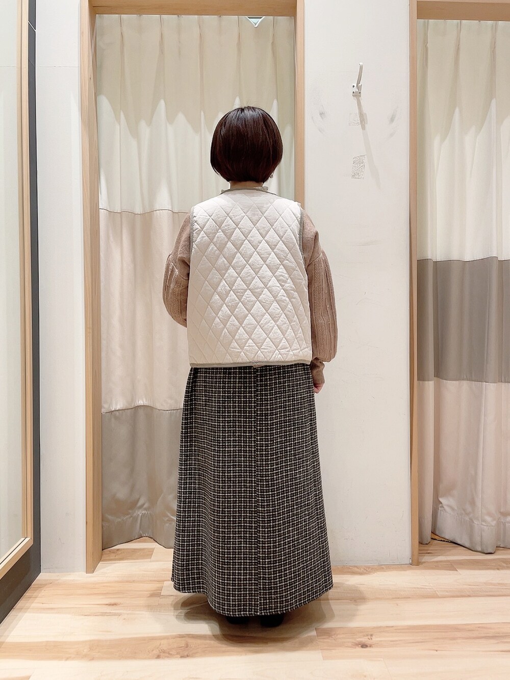 ブラウン系のスカート、ベージュ系のニット/セーター、ホワイト系のベストを着用したレディースの冬コーディネートの2枚目の写真