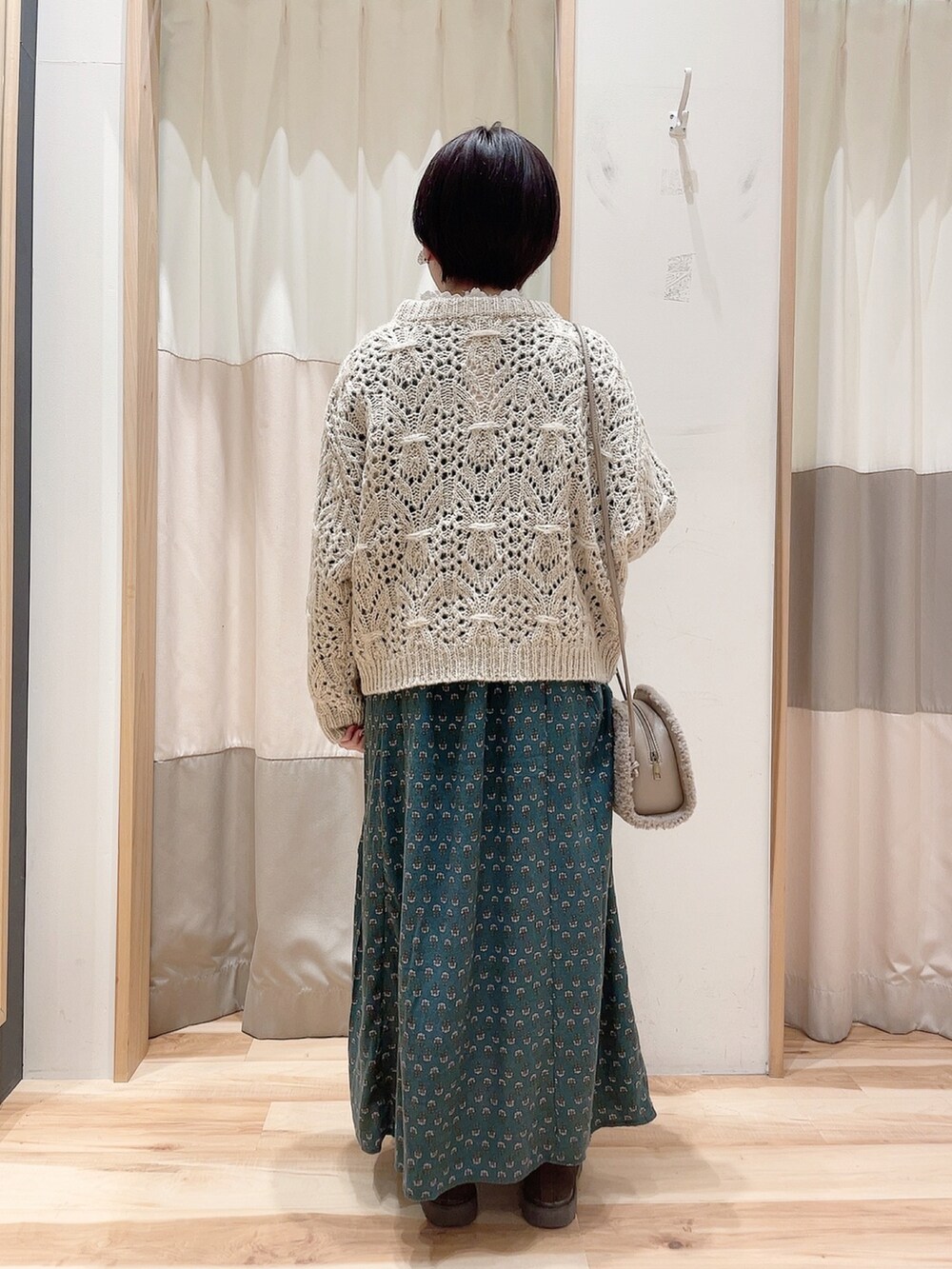 グリーン系のワンピース、ベージュ系のニット/セーター、ブラウン系のハンドバッグを着用したレディースの冬コーディネートの2枚目の写真