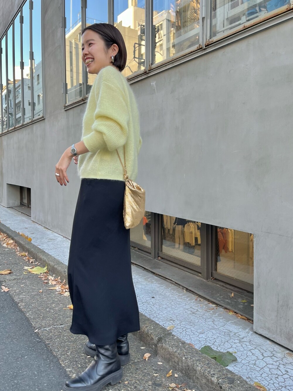 ゴールド系のクラッチバッグ、イエロー系のニット/セーター、ブラック系のスカートを着用したレディースの冬コーディネートの3枚目の写真