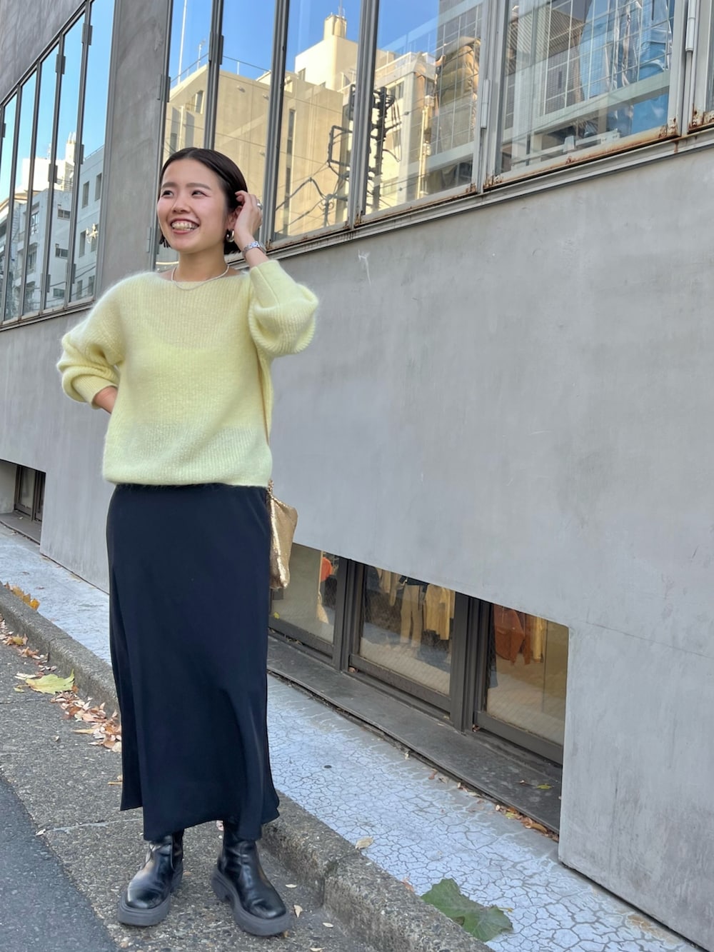 ゴールド系のクラッチバッグ、イエロー系のニット/セーター、ブラック系のスカートを着用したレディースの冬コーディネートの5枚目の写真