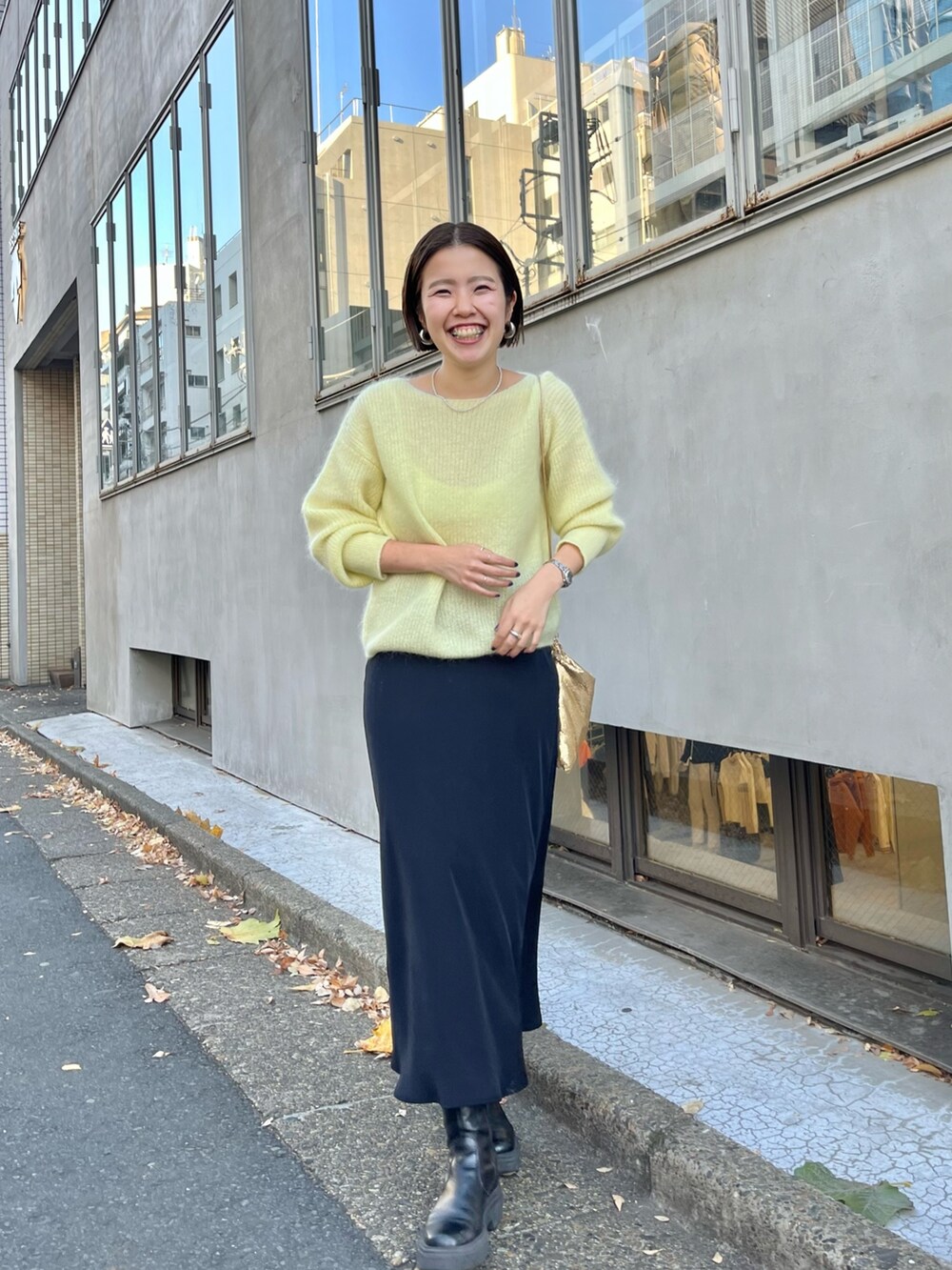 ゴールド系のクラッチバッグ、イエロー系のニット/セーター、ブラック系のスカートを着用したレディースの冬コーディネートの2枚目の写真