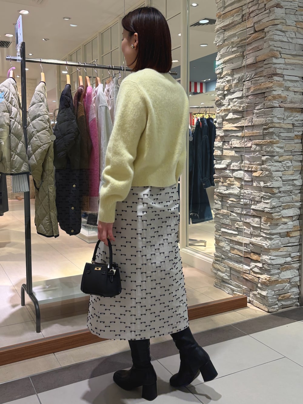 イエロー系のカーディガン/ボレロ、ベージュ系のスカート、ブラック系のショルダーバッグを着用したレディースの秋コーディネートの5枚目の写真