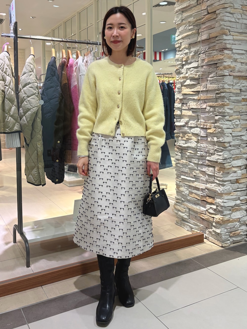 イエロー系のカーディガン/ボレロ、ベージュ系のスカート、ブラック系のショルダーバッグを着用したレディースの秋コーディネートの2枚目の写真