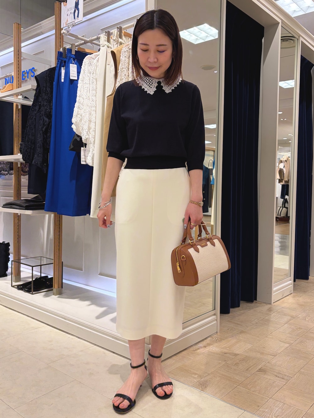 ブルー系のニット/セーター、ホワイト系のスカート、ブラウン系のボストンバッグを着用したレディースの春コーディネートの2枚目の写真