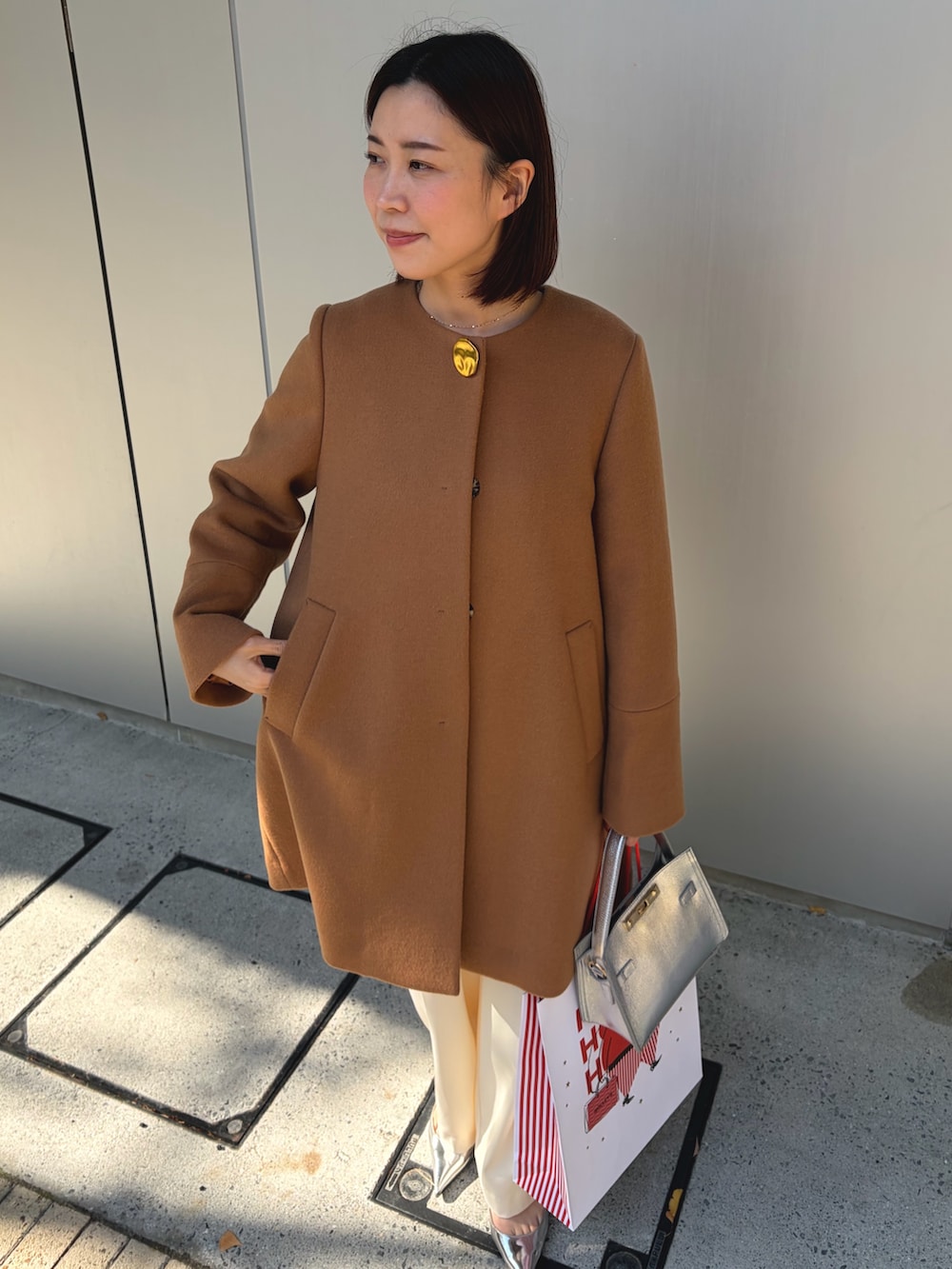 イエロー系のノーカラーコート、シルバー系のショルダーバッグ、ホワイト系のその他パンツを着用したレディースの秋コーディネートの4枚目の写真