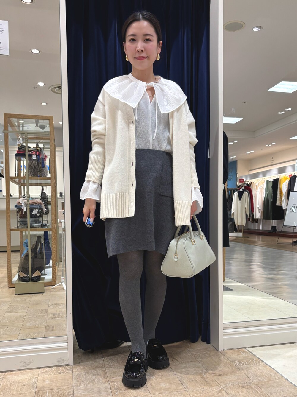 グレー系のスカート、グリーン系のショルダーバッグ、ホワイト系のカーディガン/ボレロを着用したレディースの冬コーディネートの2枚目の写真