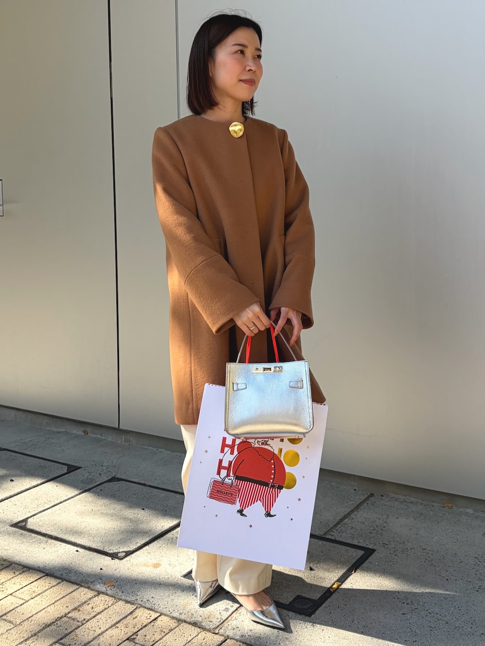 イエロー系のノーカラーコート、シルバー系のショルダーバッグ、ホワイト系のその他パンツを着用したレディースの秋コーディネートの2枚目の写真