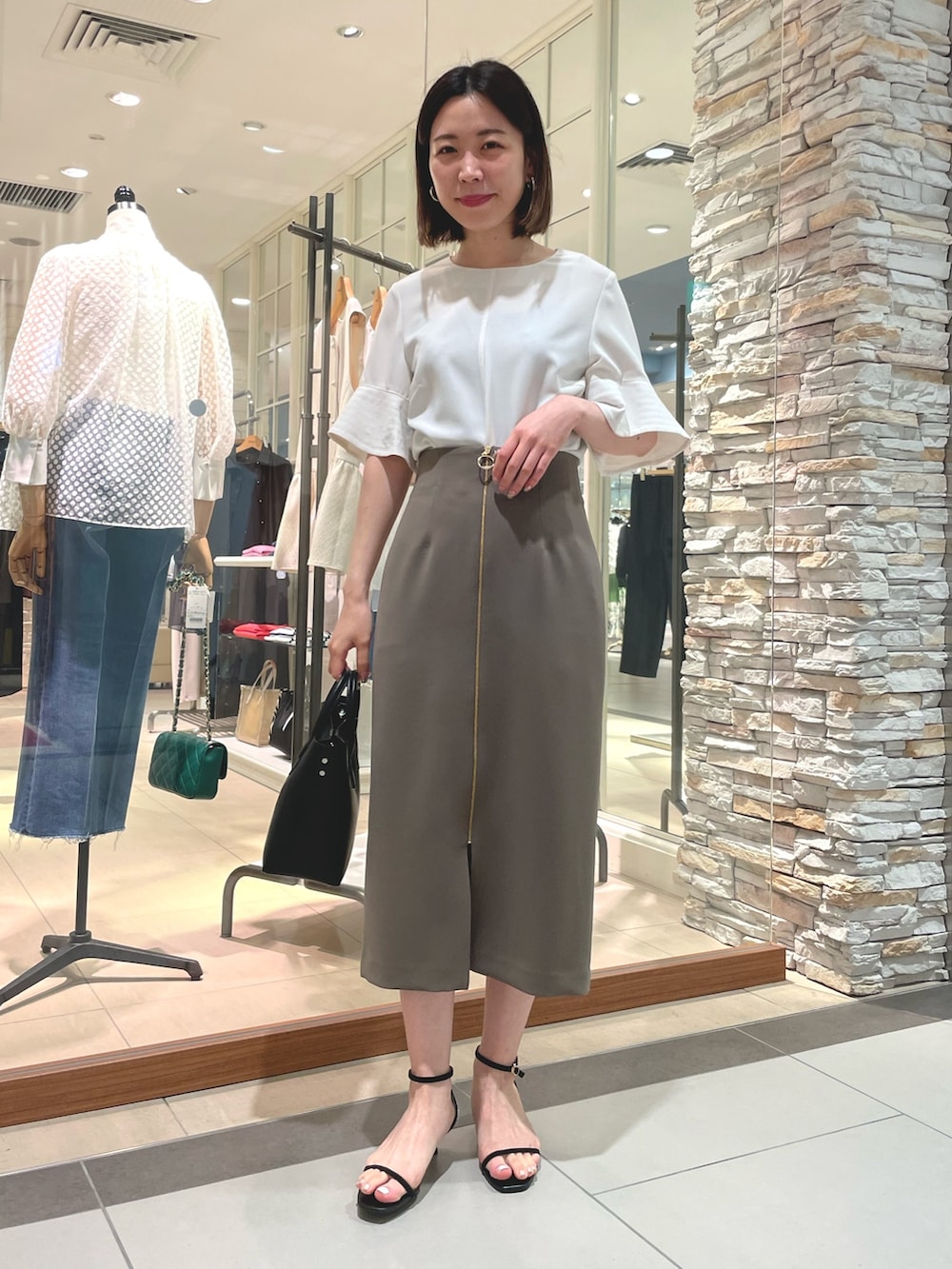 ブラック系のトートバッグ、ブラック系のサンダル、ホワイト系のシャツ/ブラウスを着用したレディースの夏コーディネートの2枚目の写真