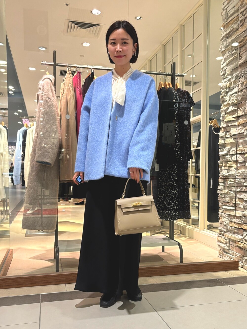 ブラック系のスカート、ベージュ系のショルダーバッグ、ブルー系のその他アウターを着用したレディースの冬コーディネートの2枚目の写真