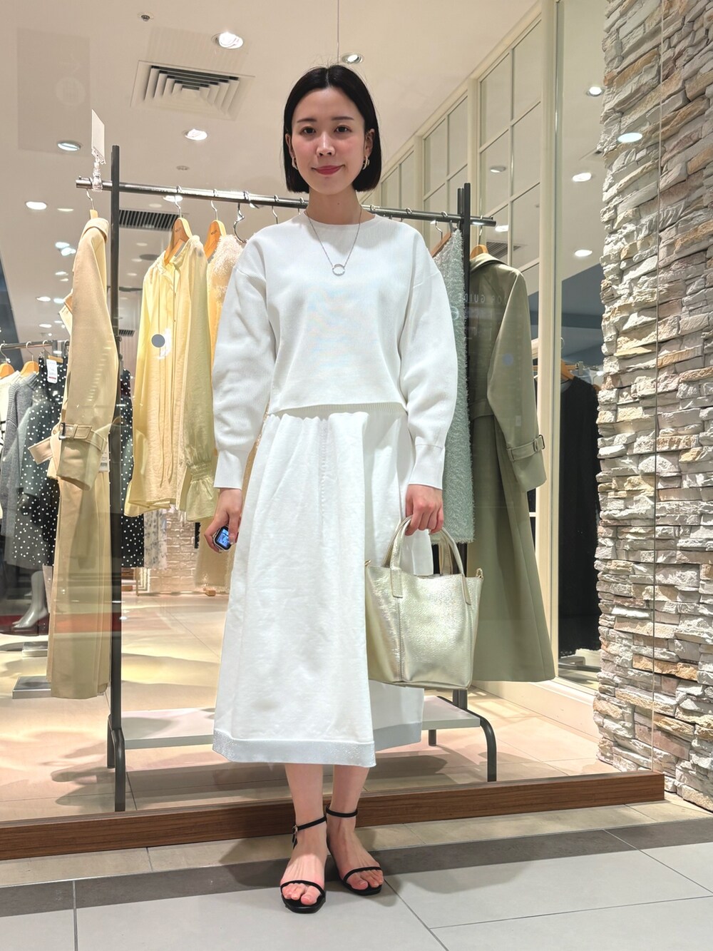 ゴールド系のトートバッグ、ホワイト系のニット/セーター、ホワイト系のスカートを着用したレディースの冬コーディネートの3枚目の写真