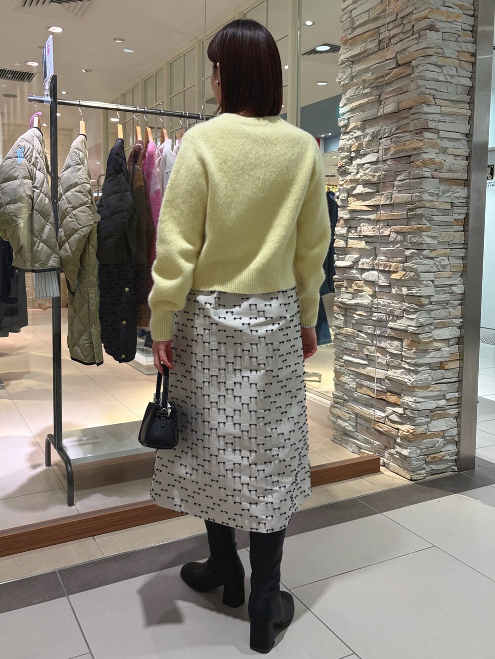 イエロー系のカーディガン/ボレロ、ベージュ系のスカート、ブラック系のショルダーバッグを着用したレディースの秋コーディネートの4枚目の写真