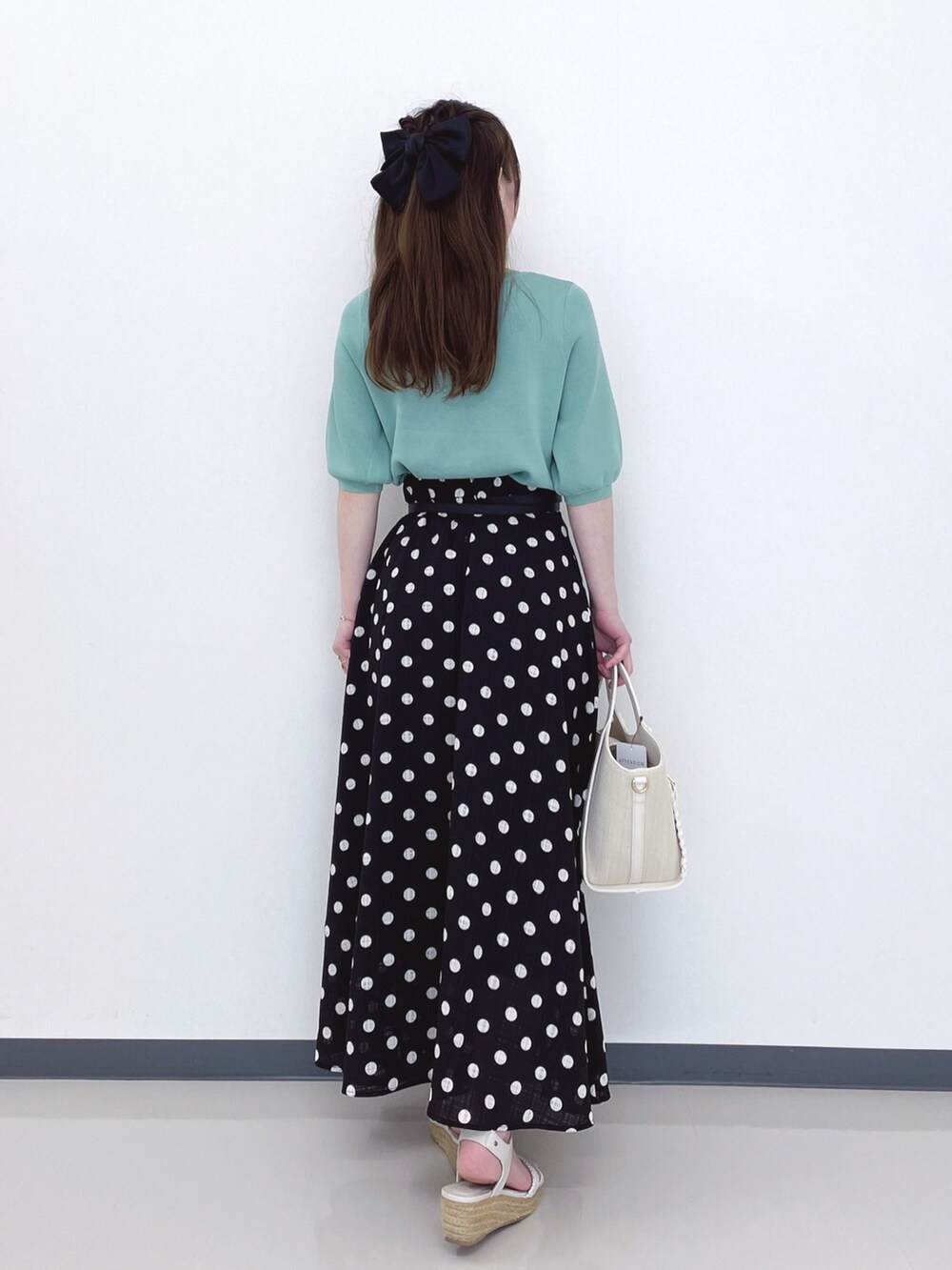 グリーン系のニット/セーター、ホワイト系のトートバッグ、ブラック系のスカートを着用したレディースの春コーディネートの3枚目の写真