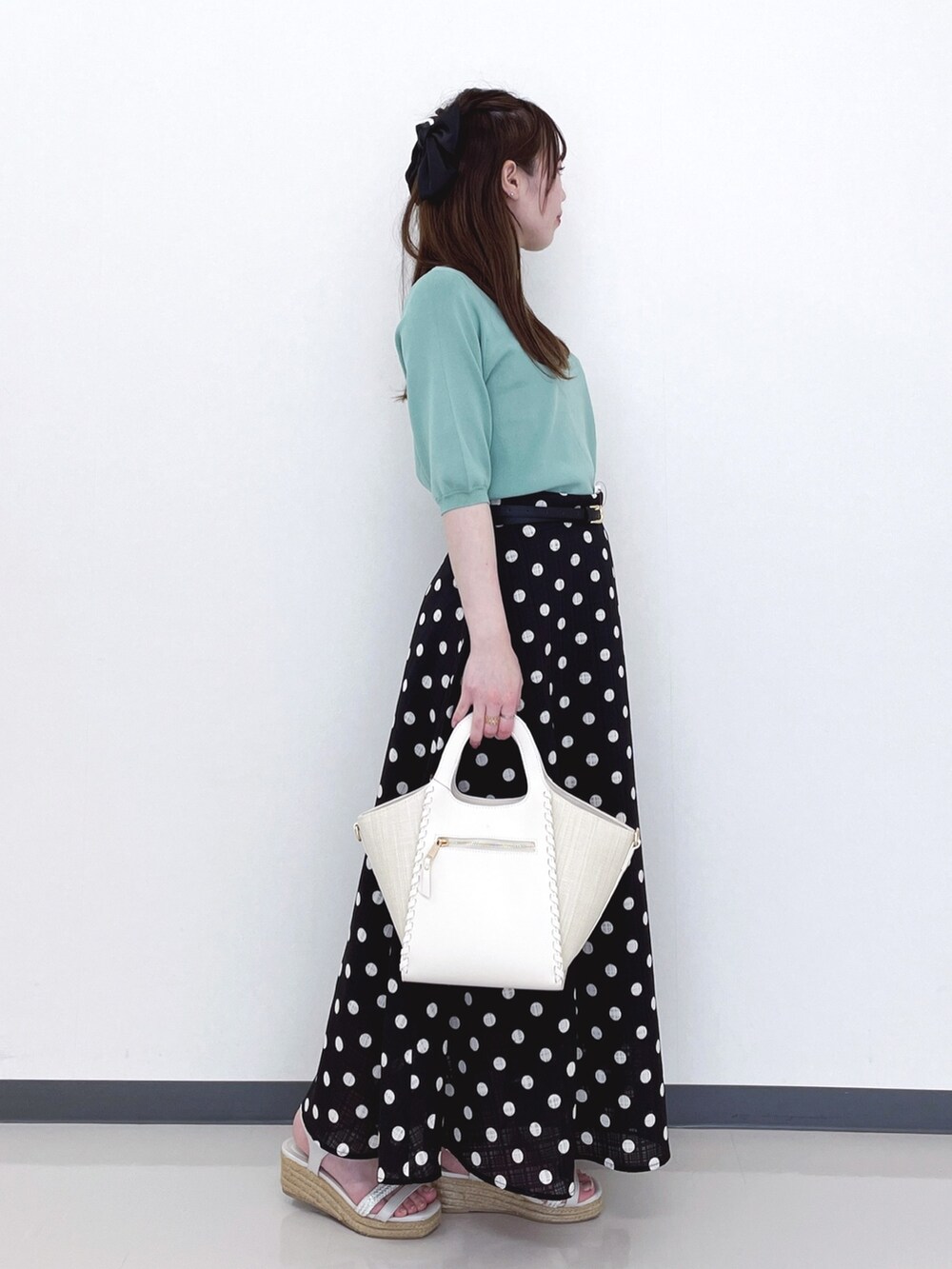 グリーン系のニット/セーター、ホワイト系のトートバッグ、ブラック系のスカートを着用したレディースの春コーディネートの2枚目の写真