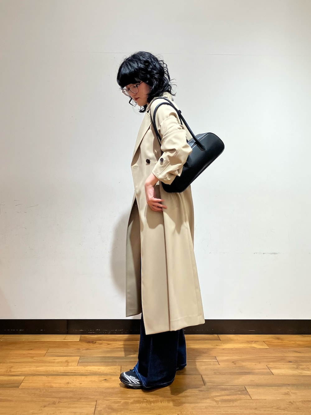 ブルー系のデニムパンツ、ベージュ系のトレンチコート、ブラック系のショルダーバッグを着用したレディースの春コーディネートの2枚目の写真