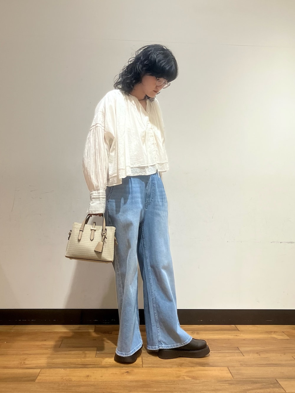 ブルー系のデニムパンツ、ベージュ系のハンドバッグ、ホワイト系のシャツ/ブラウスを着用したレディースの春コーディネートの2枚目の写真