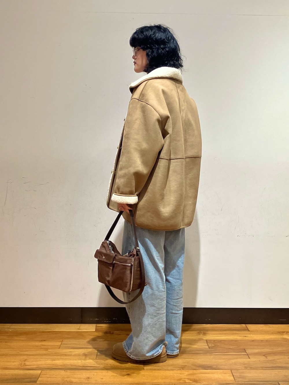 ブルー系のデニムパンツ、ブラウン系のショルダーバッグ、ホワイト系のムートンコートを着用したレディースの冬コーディネートの2枚目の写真