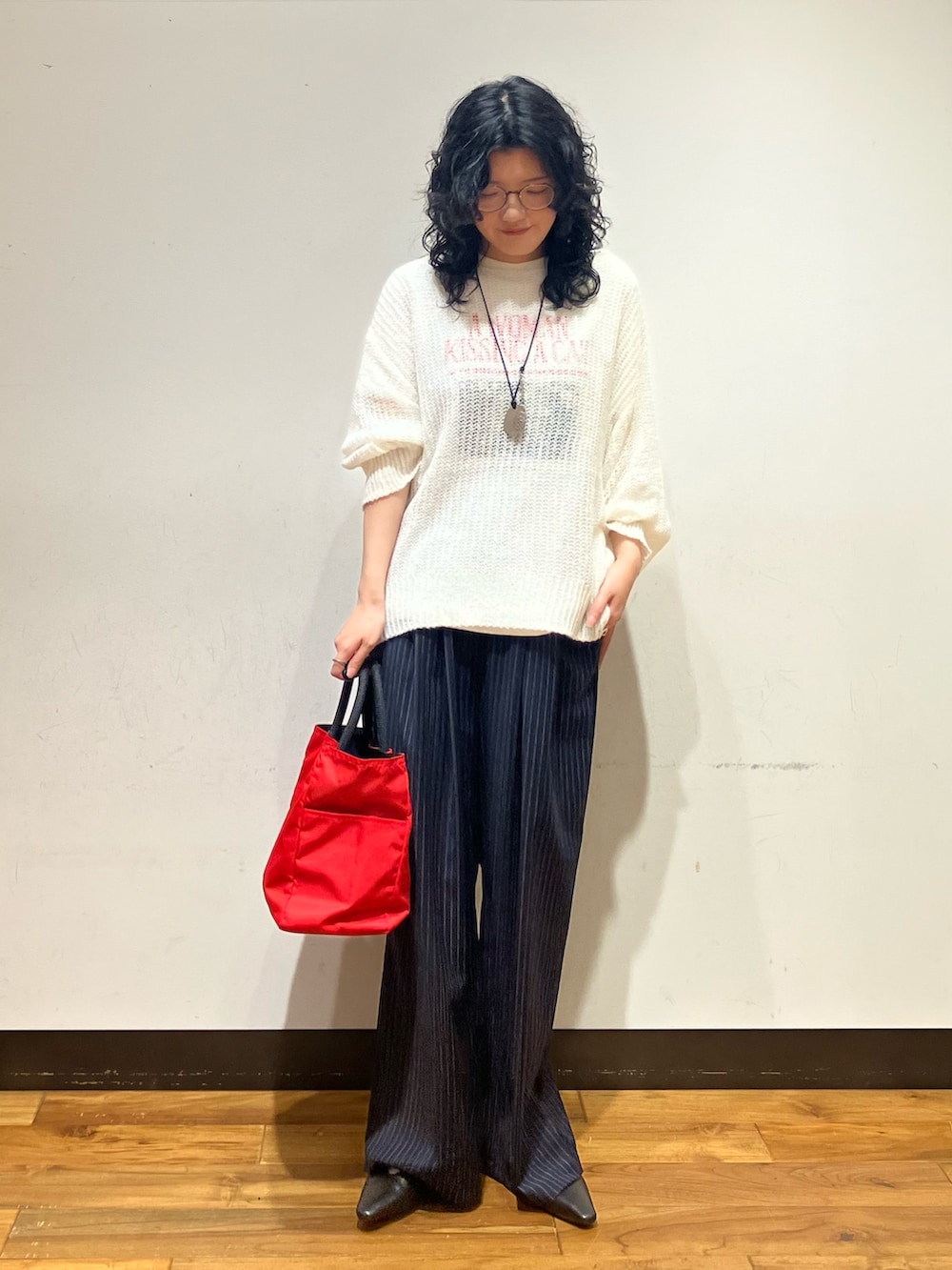 ホワイト系のニット/セーター、レッド系のトートバッグ、ホワイト系のTシャツ/カットソーを着用したレディースの秋コーディネートの2枚目の写真