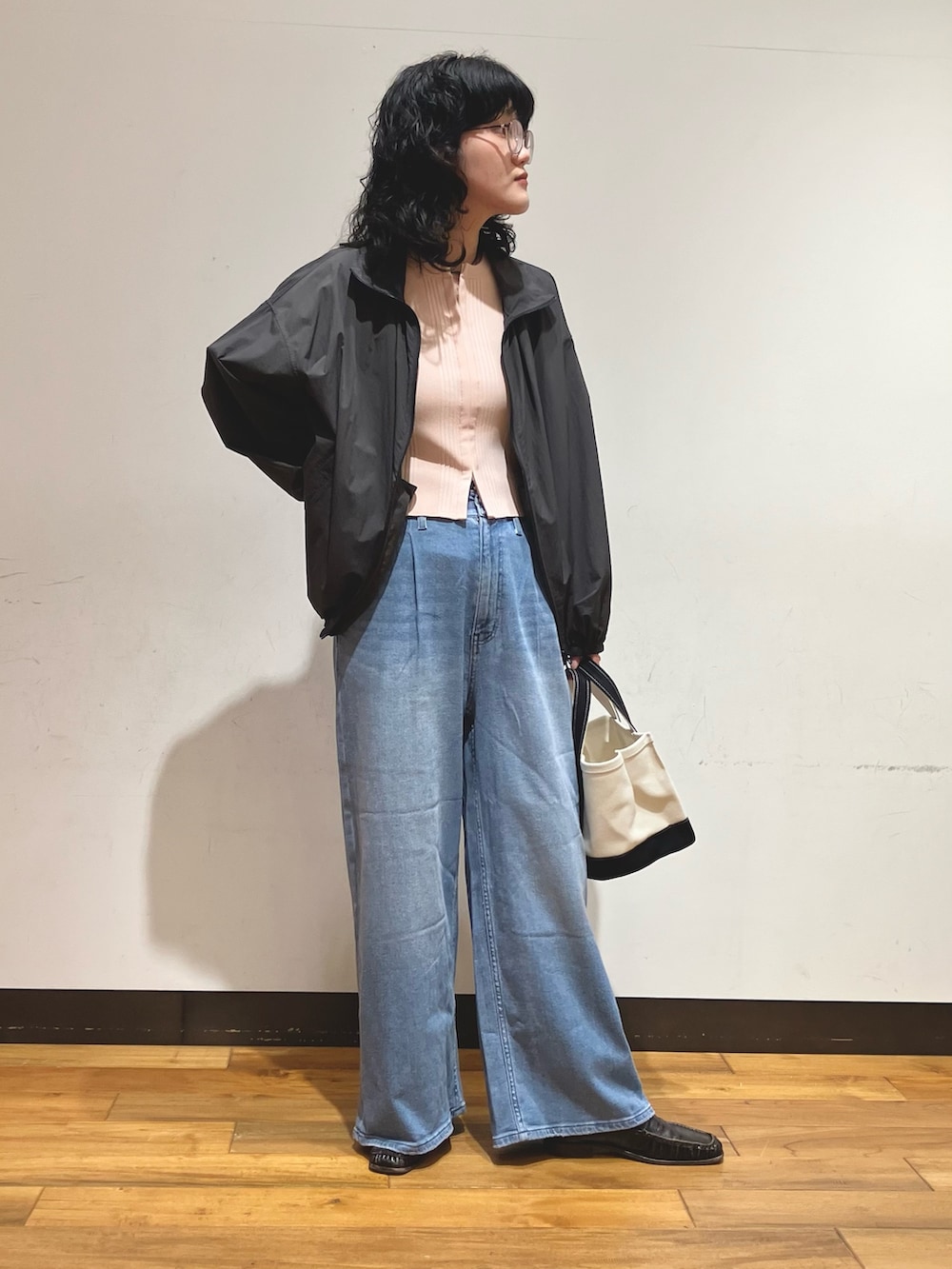 ブラック系のトートバッグ、ブルー系のデニムパンツ、グレー系のブルゾンを着用したレディースの春コーディネートの2枚目の写真