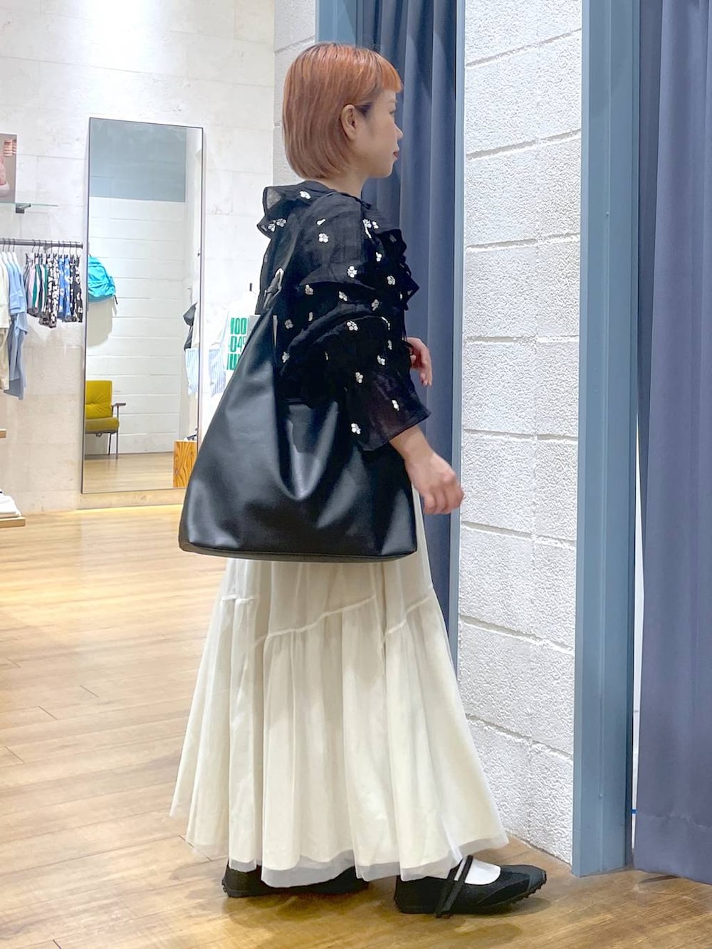 ブラック系のショルダーバッグ、ブラック系のスニーカー、ホワイト系のスカートを着用したレディースの春コーディネートの2枚目の写真