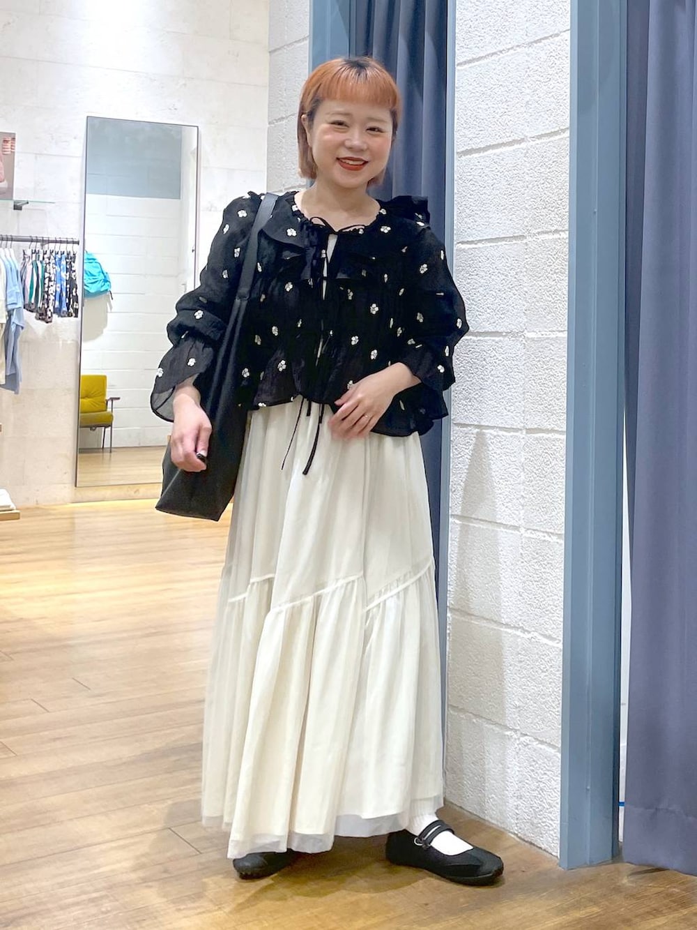 ブラック系のショルダーバッグ、ブラック系のスニーカー、ホワイト系のスカートを着用したレディースの春コーディネートの3枚目の写真