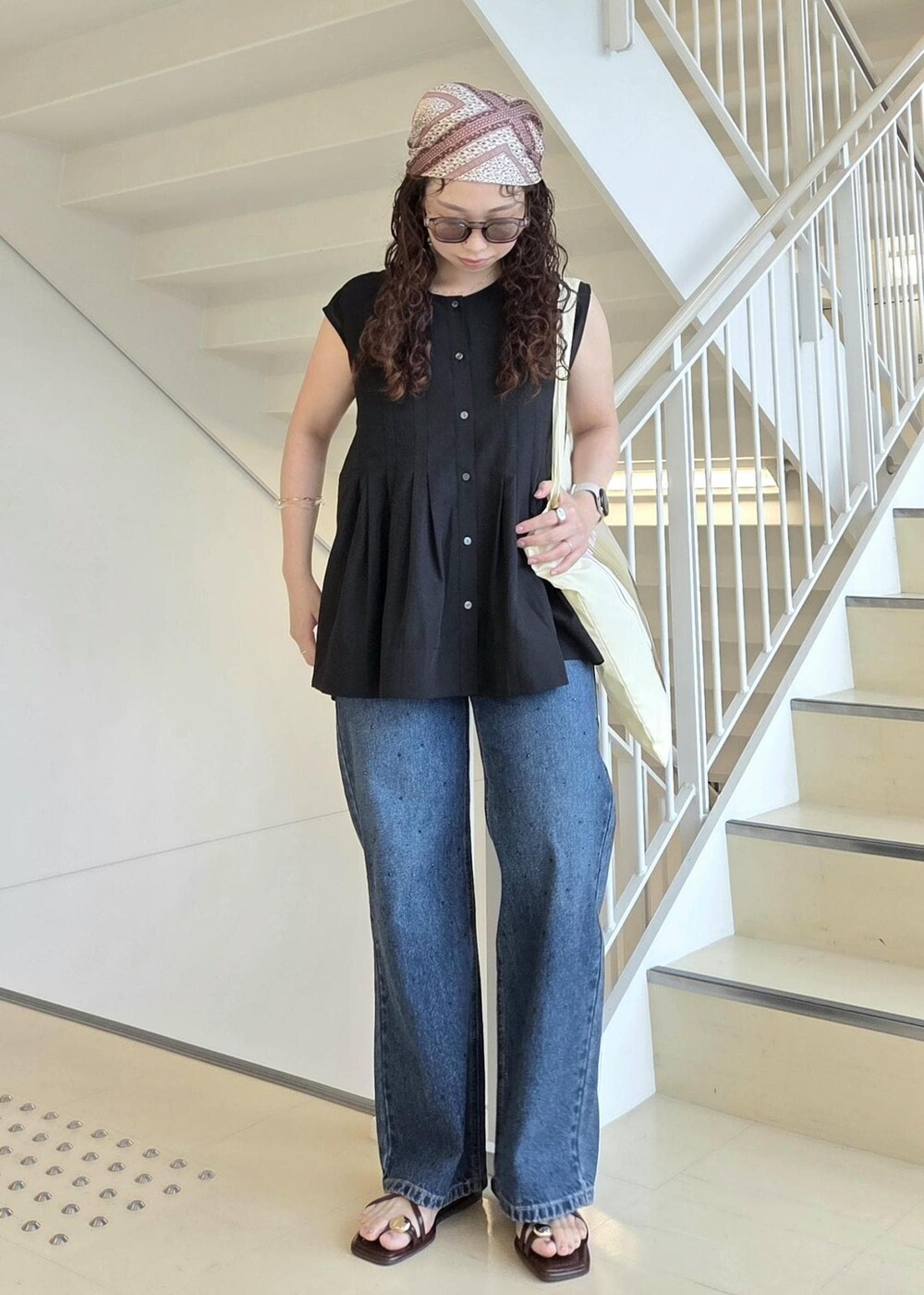 ブルー系のデニムパンツ、ブラック系のサンダル、イエロー系のトートバッグを着用したレディースの夏コーディネートの3枚目の写真