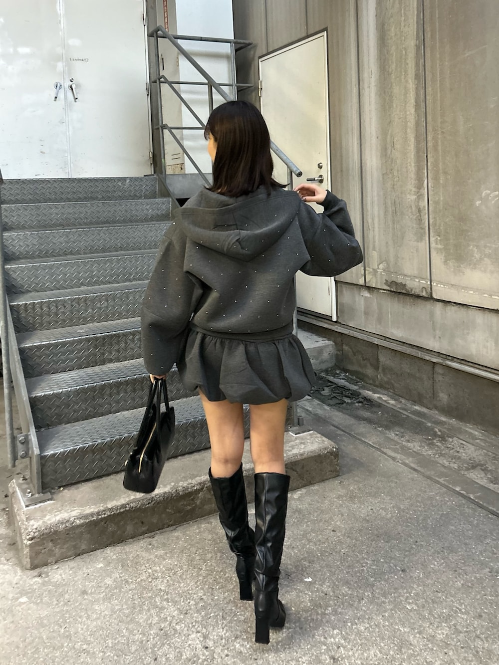 グレー系のパーカー、グレー系のスカート、ブラック系のボストンバッグを着用したレディースの秋コーディネートの2枚目の写真