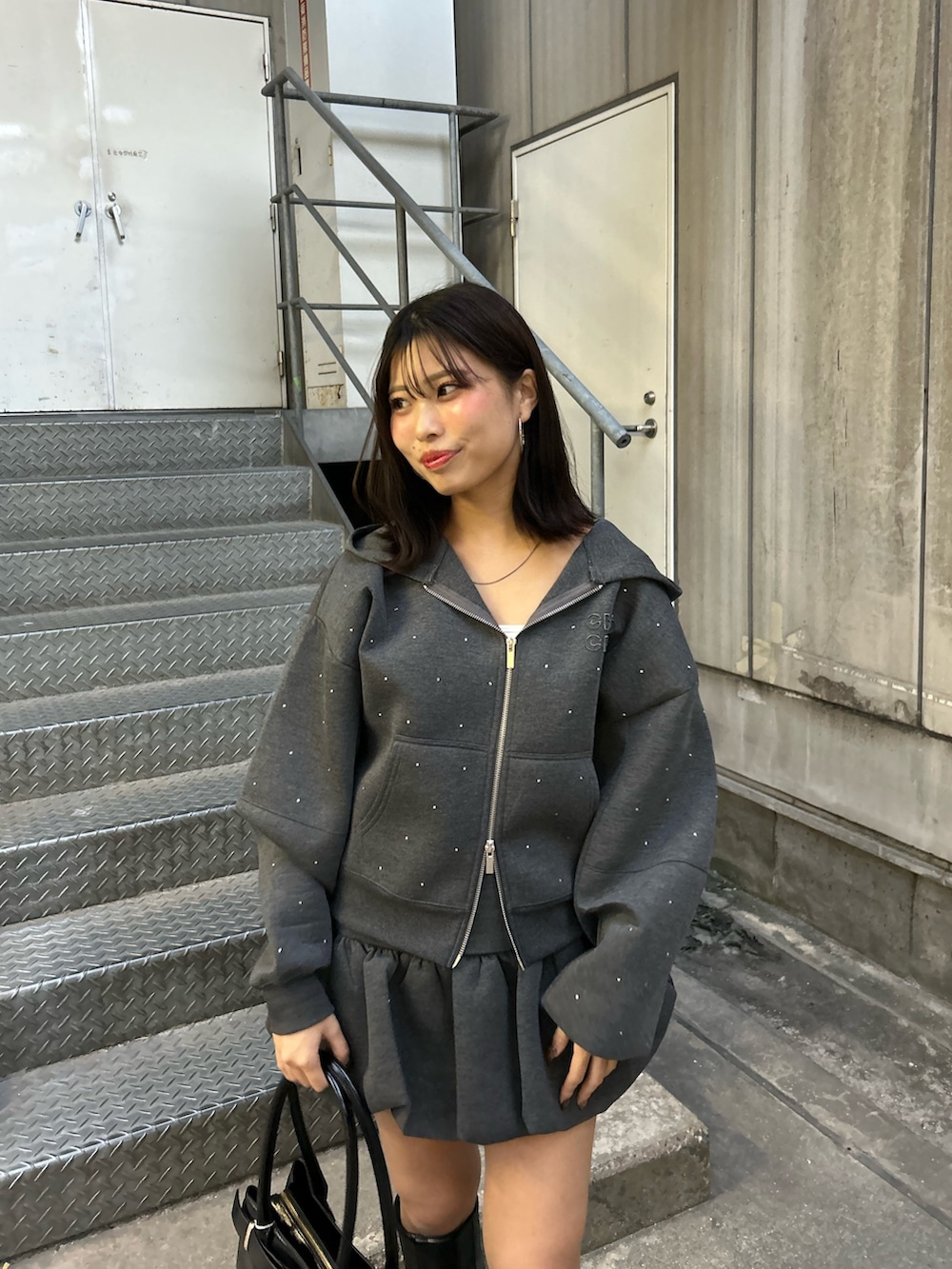 グレー系のパーカー、グレー系のスカート、ブラック系のボストンバッグを着用したレディースの秋コーディネートの3枚目の写真