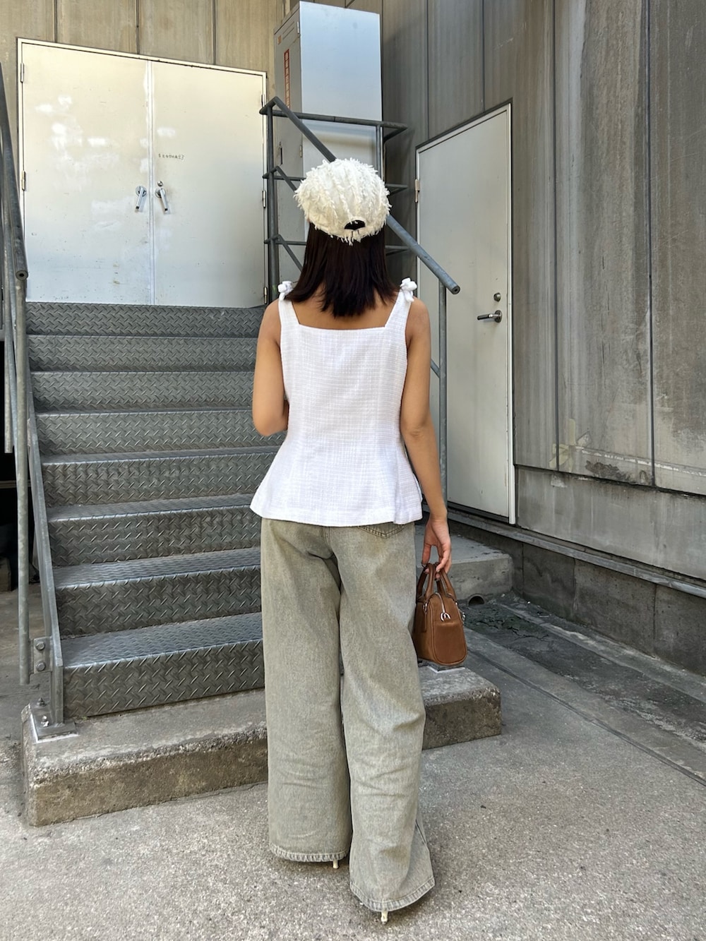 ホワイト系のベスト、ブルー系のデニムパンツ、ブラウン系のボストンバッグを着用したレディースの夏コーディネートの3枚目の写真