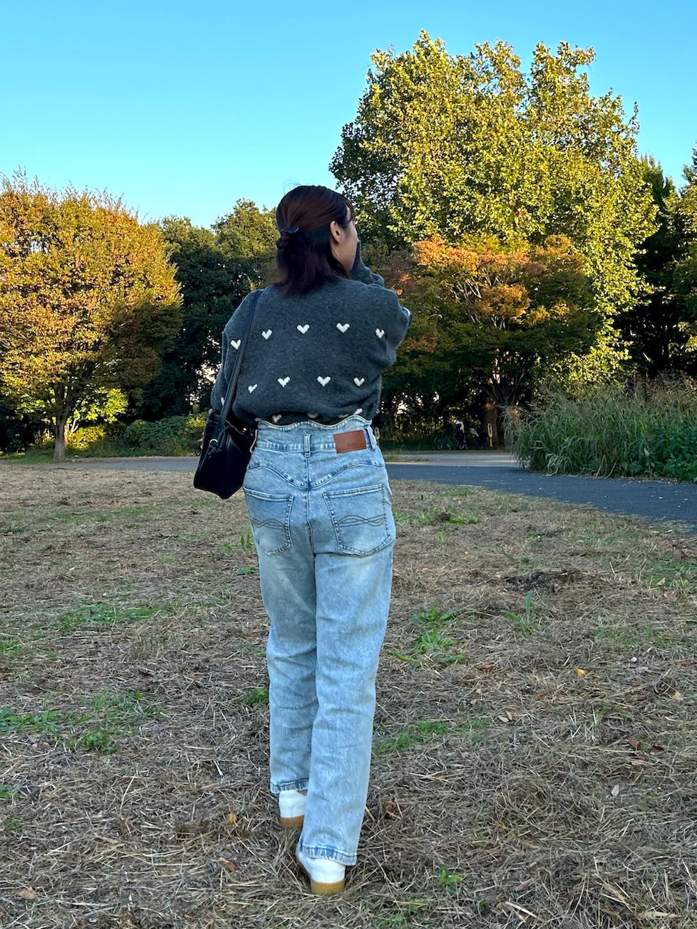 グレー系のニット/セーター、ブルー系のデニムパンツ、ブラック系のショルダーバッグを着用したレディースの秋コーディネートの2枚目の写真