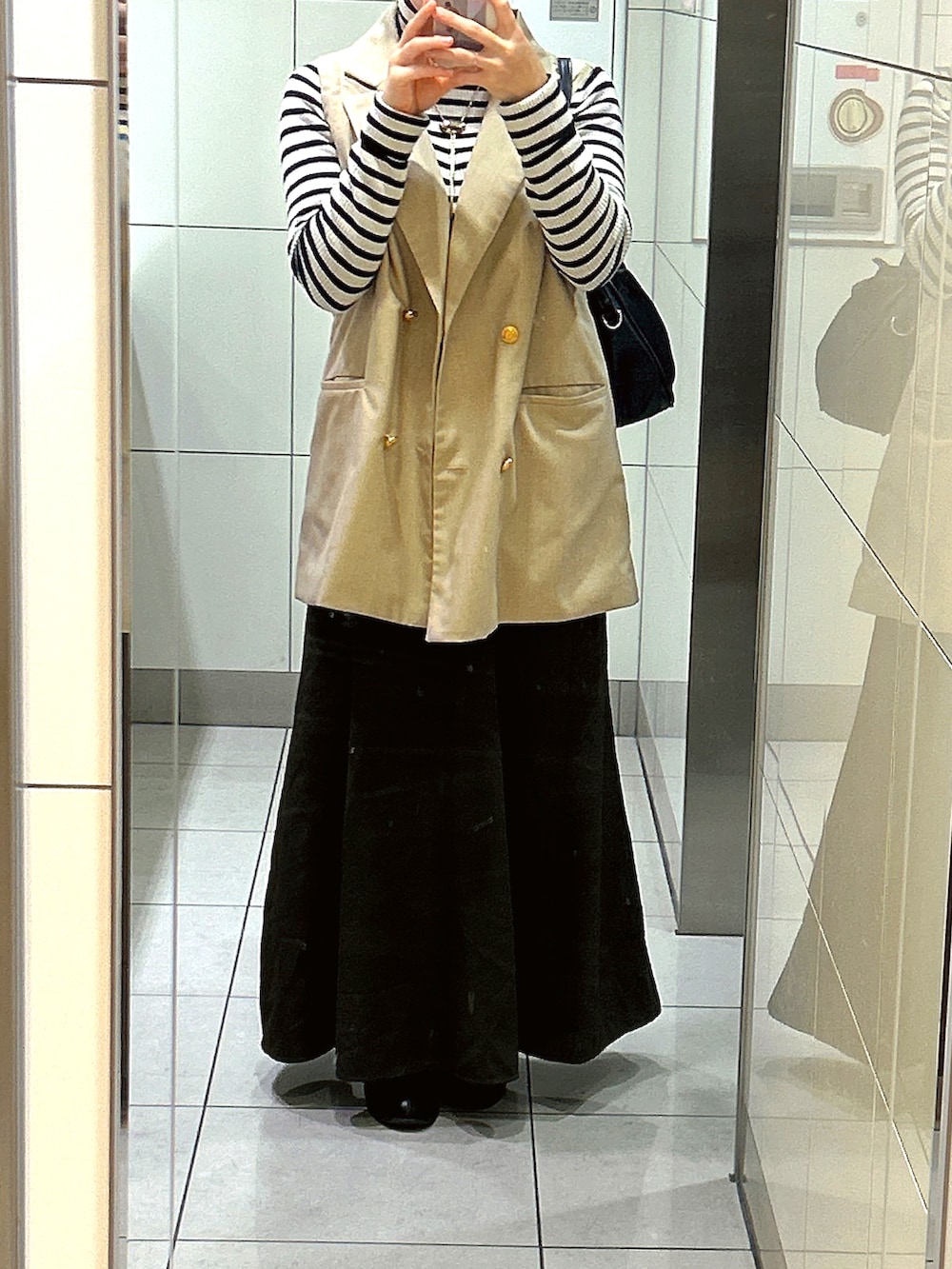 ブラック系のショルダーバッグ、ブラウン系のスカート、ブラック系のブーツを着用したレディースの秋コーディネートの2枚目の写真