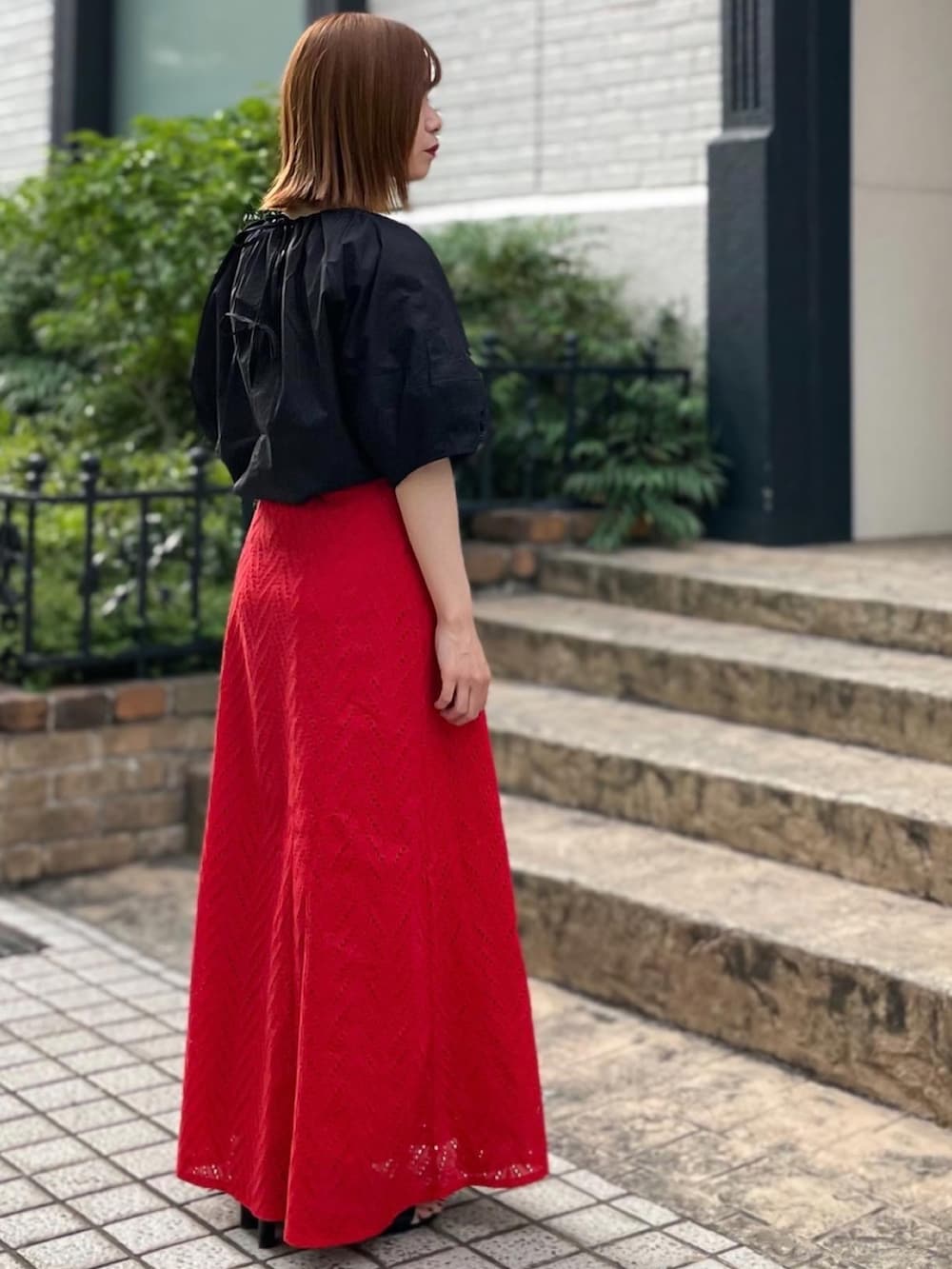 レッド系のスカート、ブラック系のシャツ/ブラウス、ブラック系のショルダーバッグを着用したレディースの夏コーディネートの2枚目の写真
