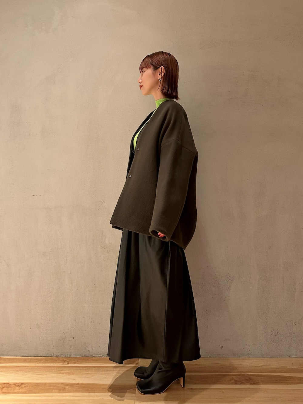 ブラック系のジャンパースカート、ブラック系のブーツ、グリーン系のニット/セーターを着用したレディースの秋コーディネートの3枚目の写真