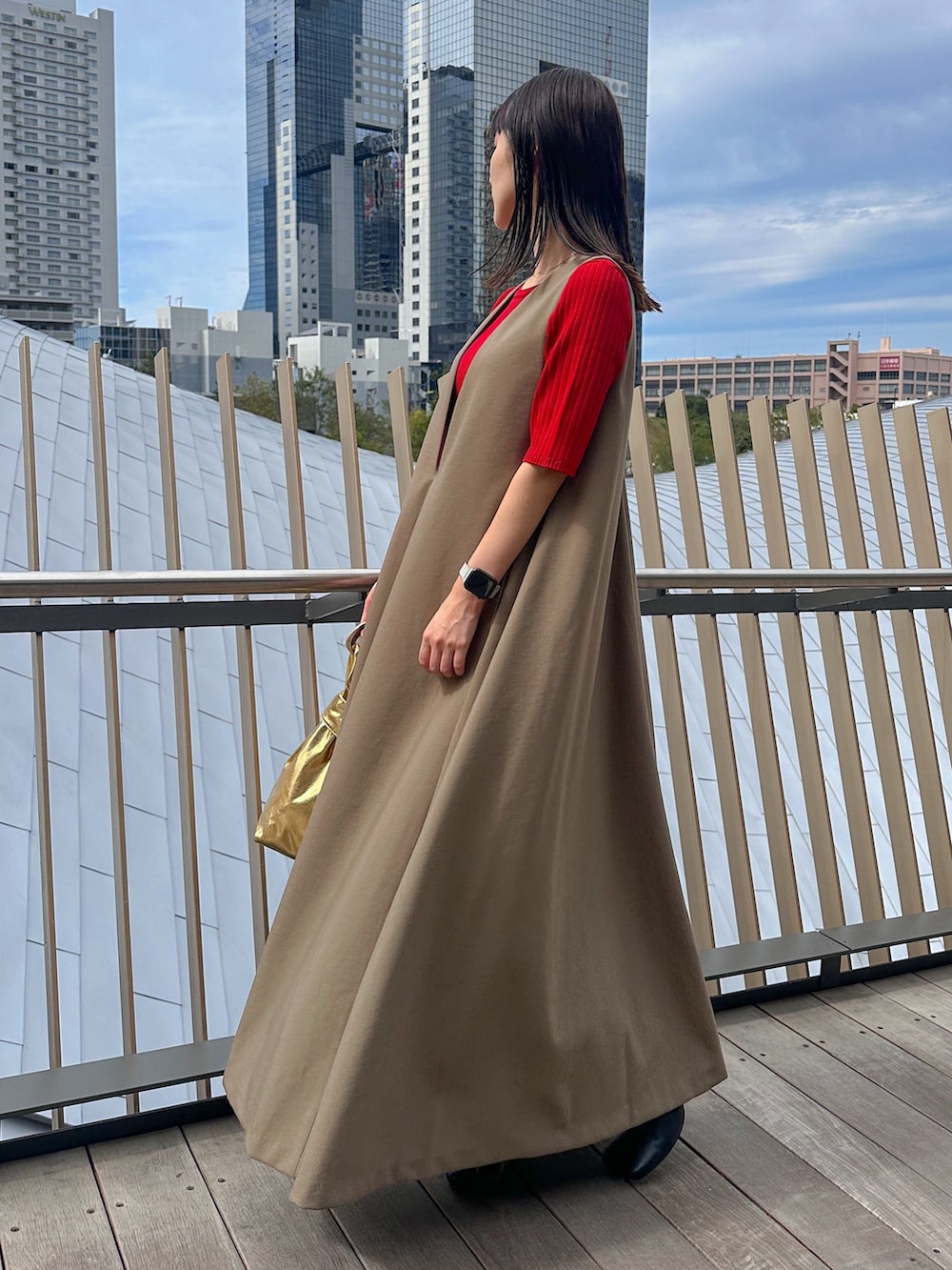 レッド系のニット/セーター、ゴールド系のハンドバッグ、ブラック系のブーツを着用したレディースの秋コーディネートの2枚目の写真