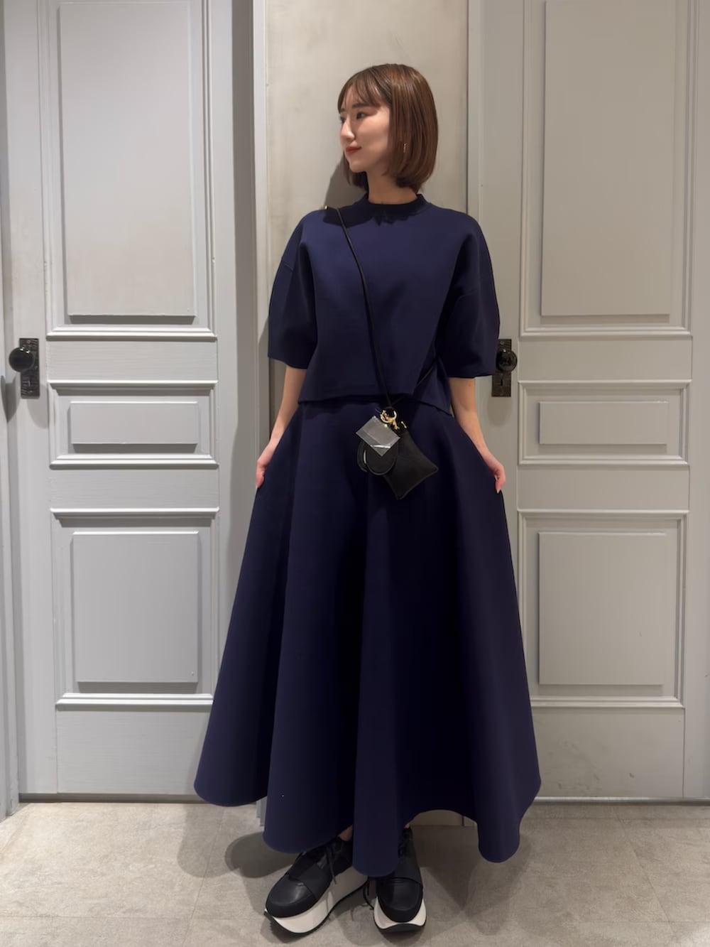 ブルー系のニット/セーター、ブルー系のスカート、ブラック系のスマホグッズを着用したレディースの春コーディネートの2枚目の写真