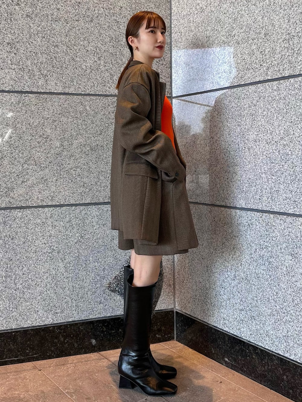 オレンジ系のニット/セーター、ブラウン系のテーラードジャケット、ブラウン系のスカートを着用したレディースの秋コーディネートの2枚目の写真