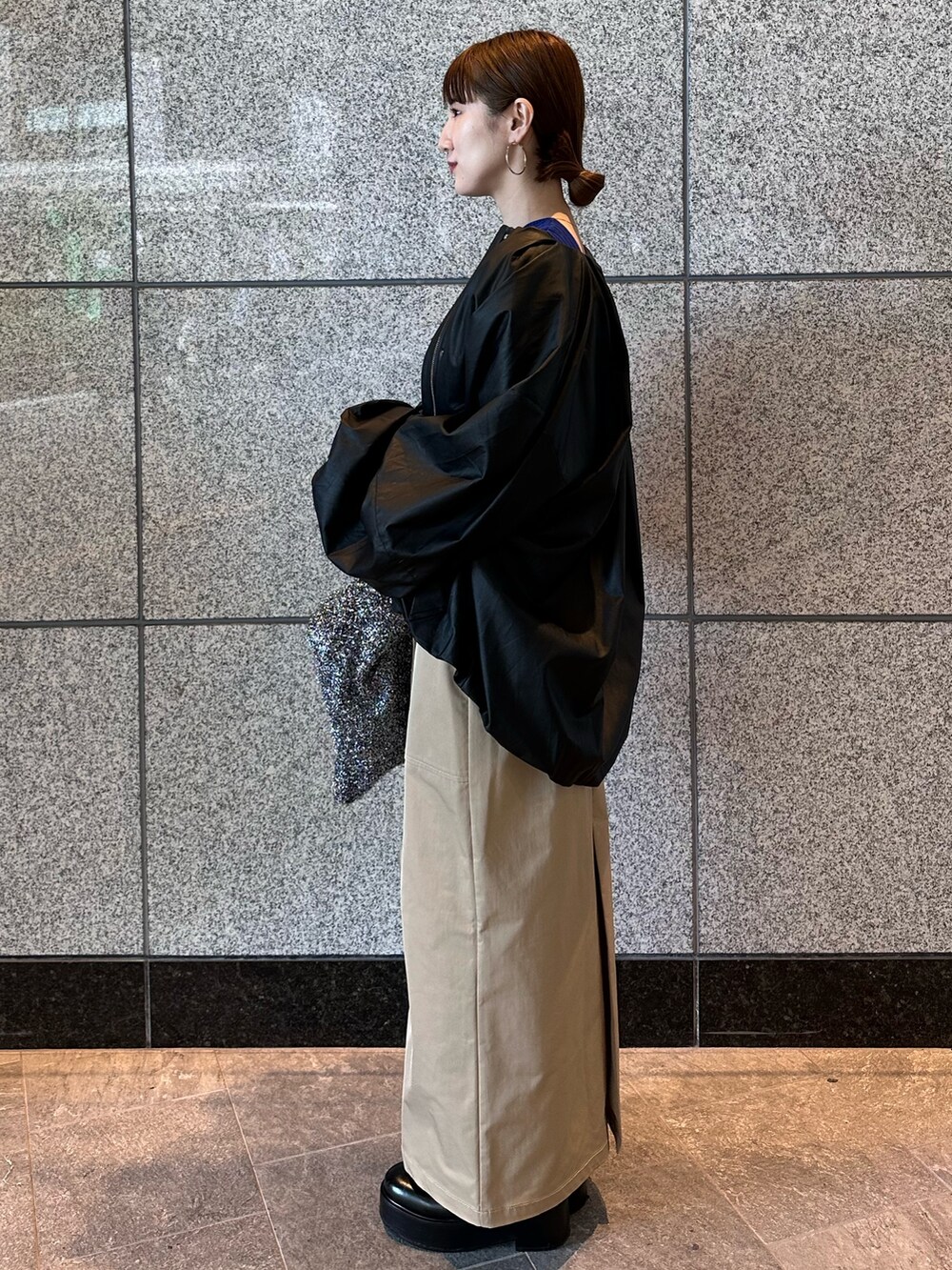 ブルー系のニット/セーター、ブラック系のノーカラージャケット、ベージュ系のスカートを着用したレディースの秋コーディネートの6枚目の写真