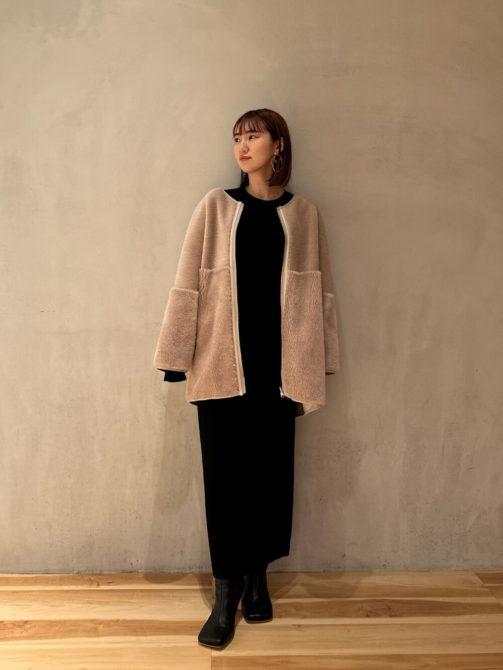 ブラック系のスカート、ブラック系のブーツ、ベージュ系のノーカラーコートを着用したレディースの夏コーディネートの2枚目の写真